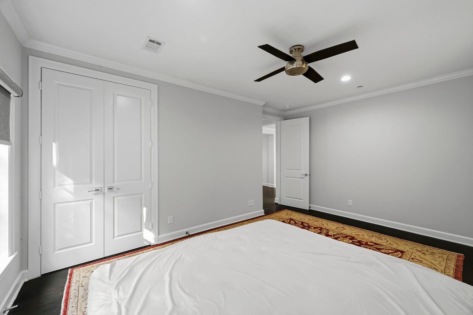 Spacious bedroom with elegant double doors, sleek ceiling fan, and rich floors, offering a modern and inviting atmosphere.