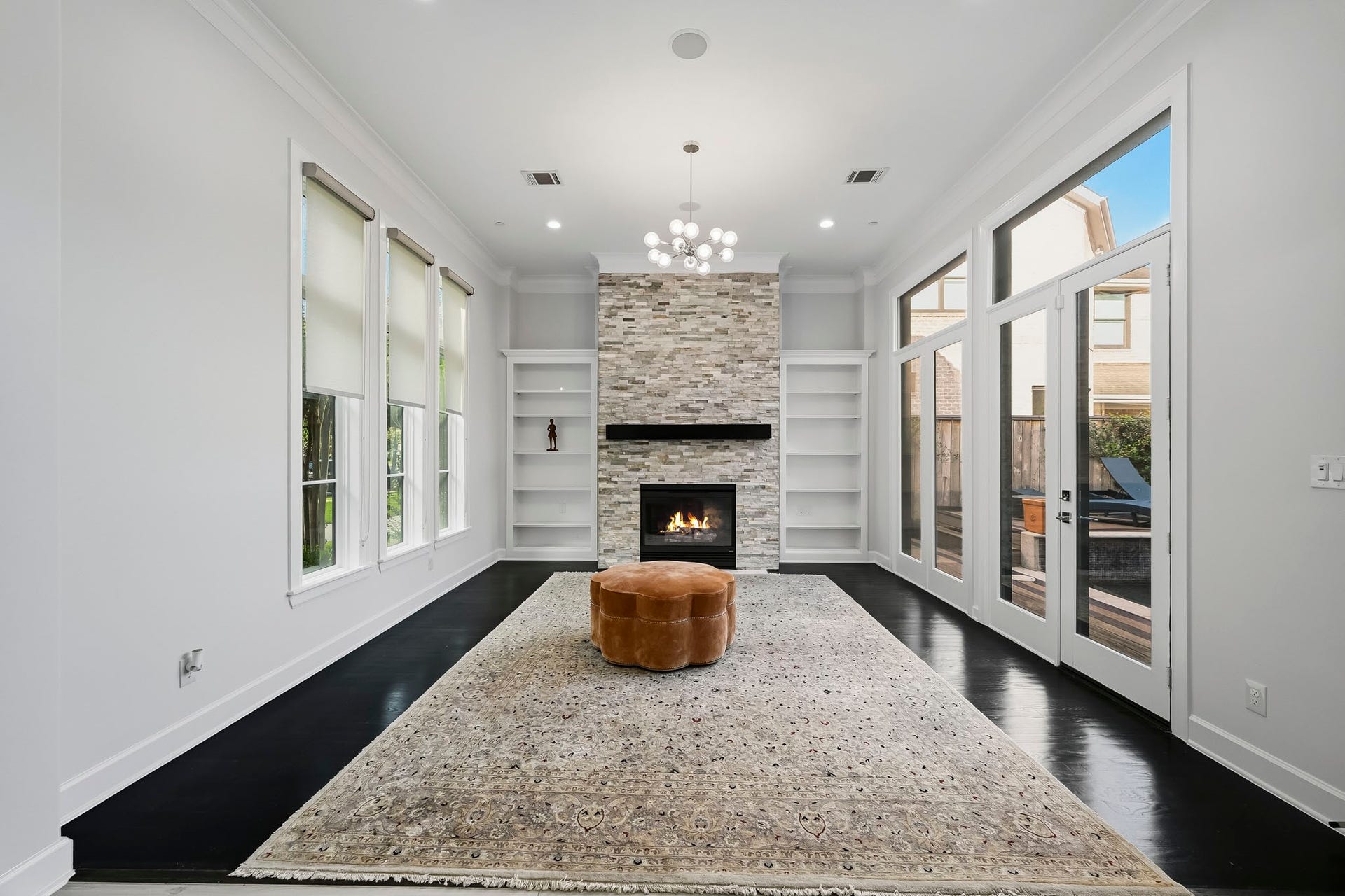 Elegant living space featuring a modern stone fireplace, expansive windows, and sleek dark flooring, creating a bright and inviting space.
