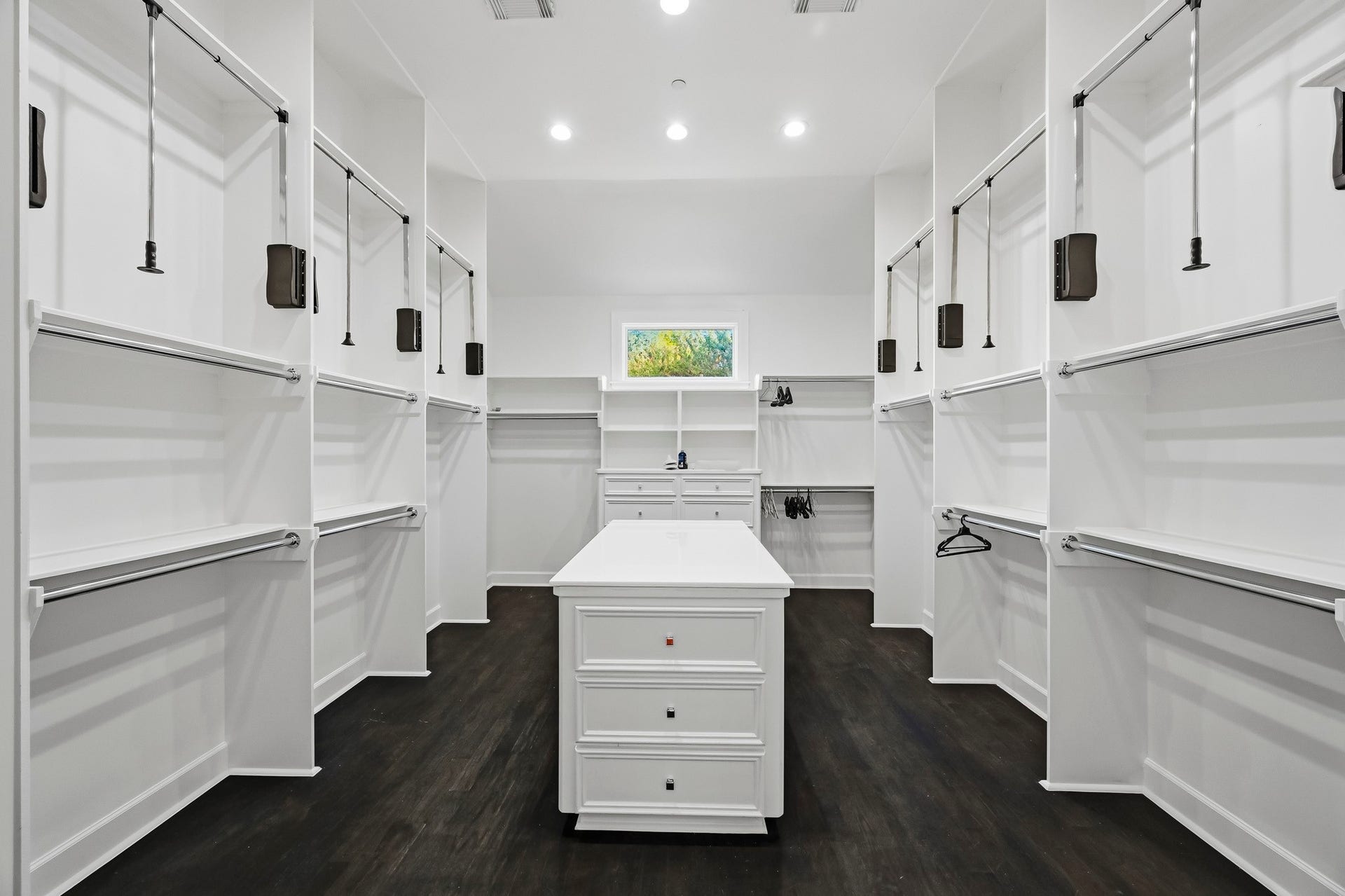 Spacious primary walk-in closet featuring sleek white cabinetry, ample hanging space, and a central island for added convenience and organization.