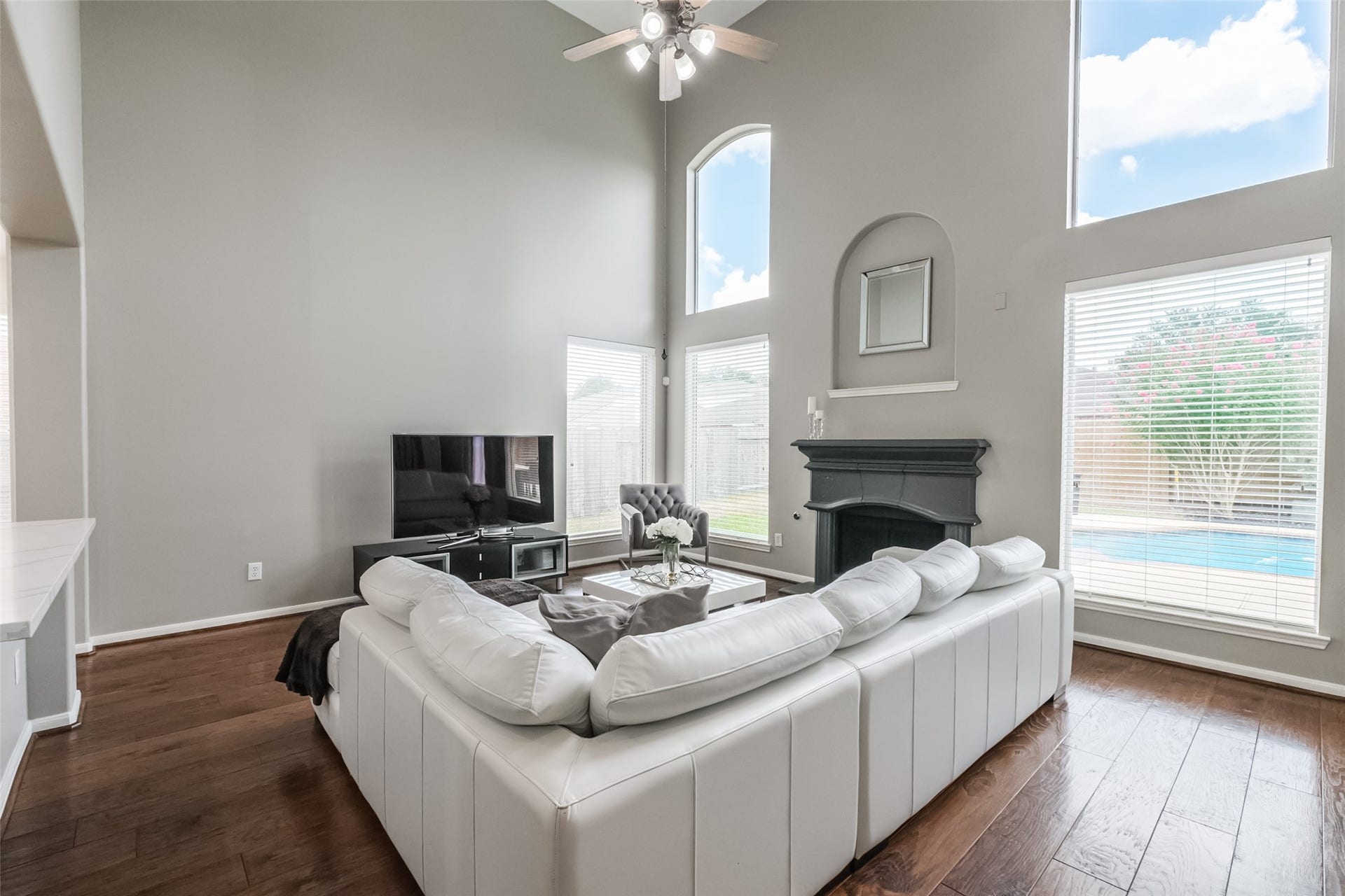10314 Five Oaks Crossing, Missouri City, TX 77459 This spacious living room features high ceilings, hardwood floors, and large windows offering plenty of natural light. It includes a cozy fireplace and a view of the pool outside, creating an inviting atmosphere for relaxation and entertainment.