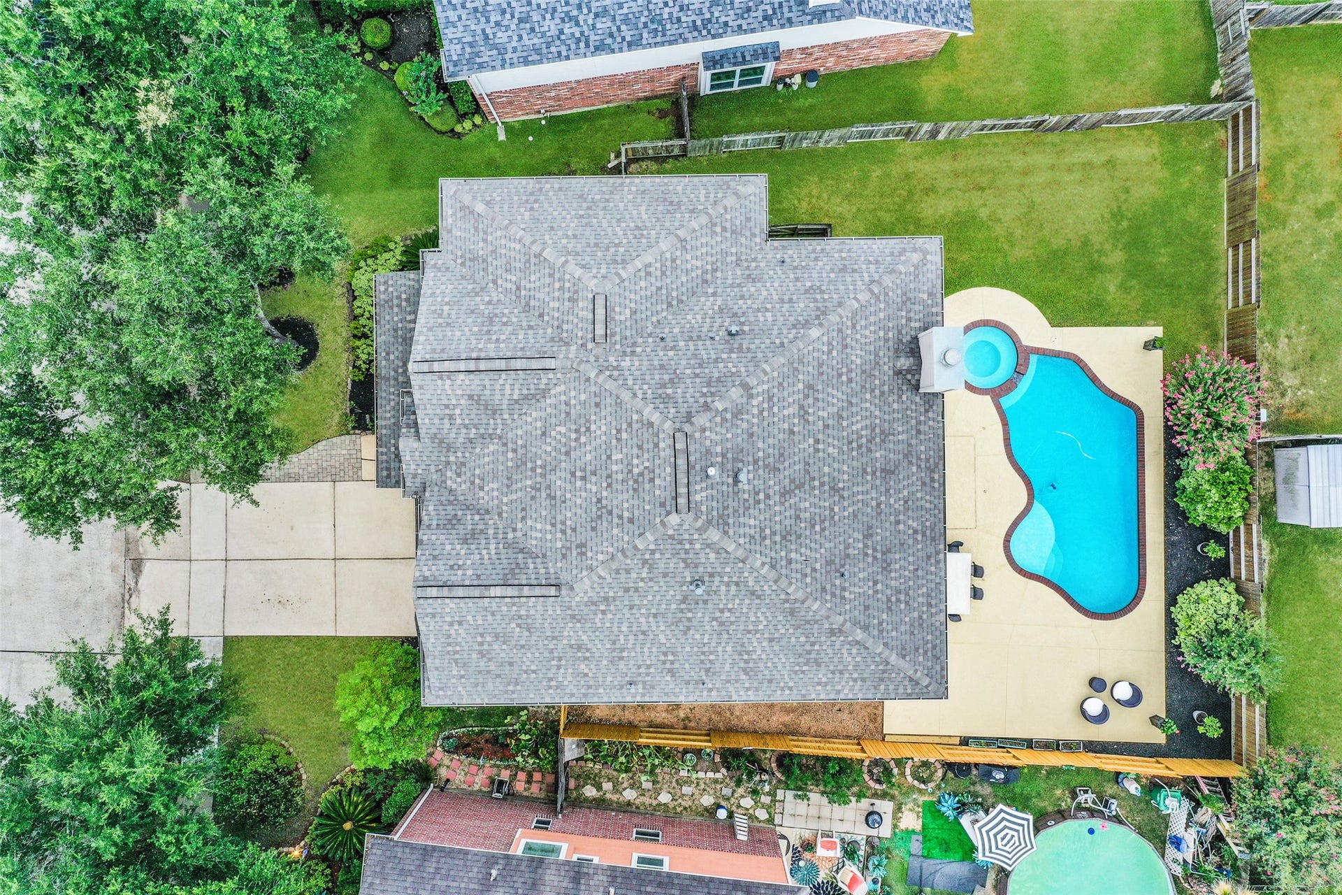 10314 Five Oaks Crossing, Missouri City, TX 77459 This aerial view showcases a well-maintained home with a spacious backyard, featuring a uniquely shaped pool and spa. The property is bordered by a lush green lawn and mature trees, providing privacy and a serene outdoor space.