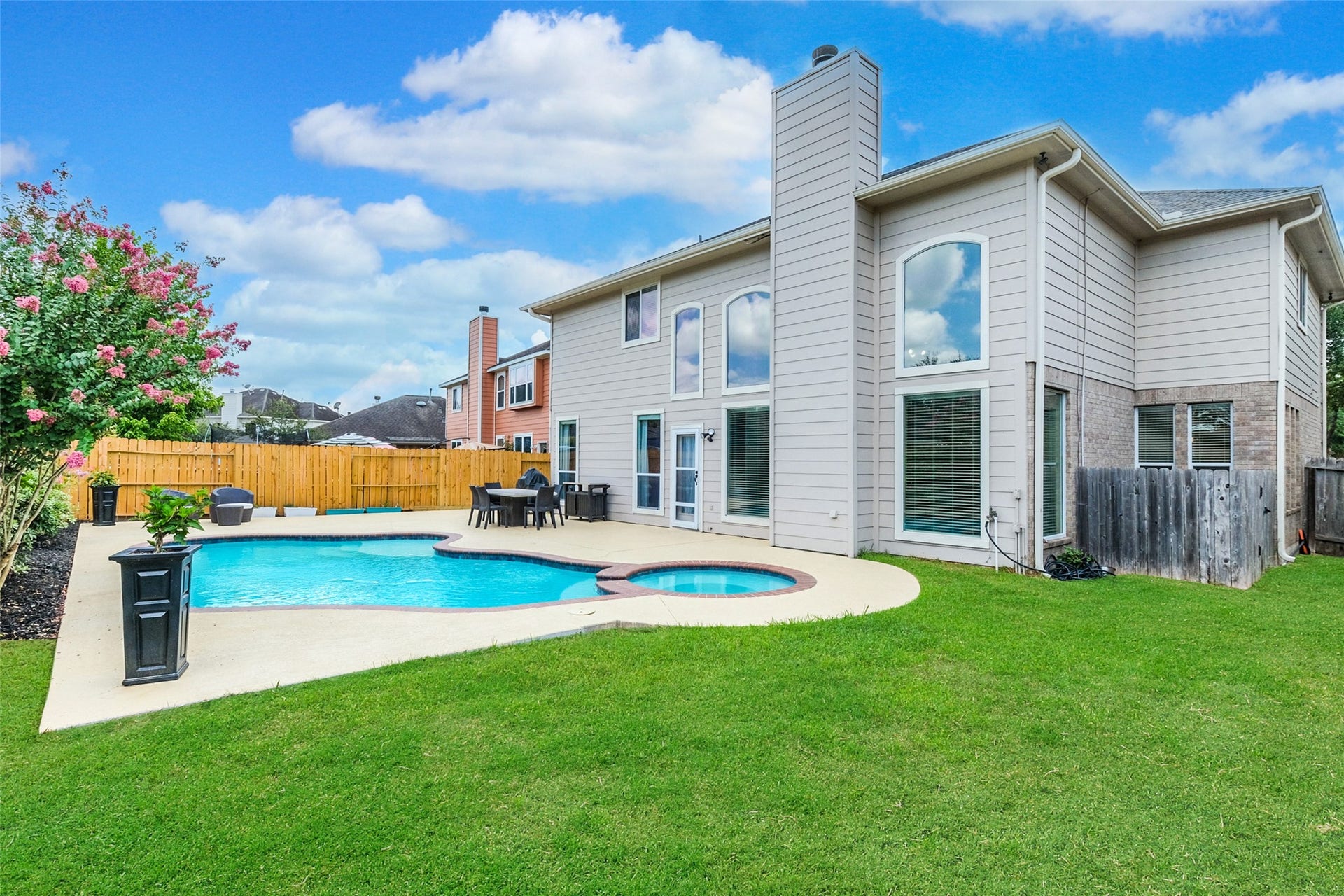 10314 Five Oaks Crossing, Missouri City, TX 77459 This spacious backyard features a pristine pool and hot tub, surrounded by a well-maintained lawn and privacy fence. The modern two-story home has large windows, offering plenty of natural light. Perfect for outdoor entertaining and relaxation.