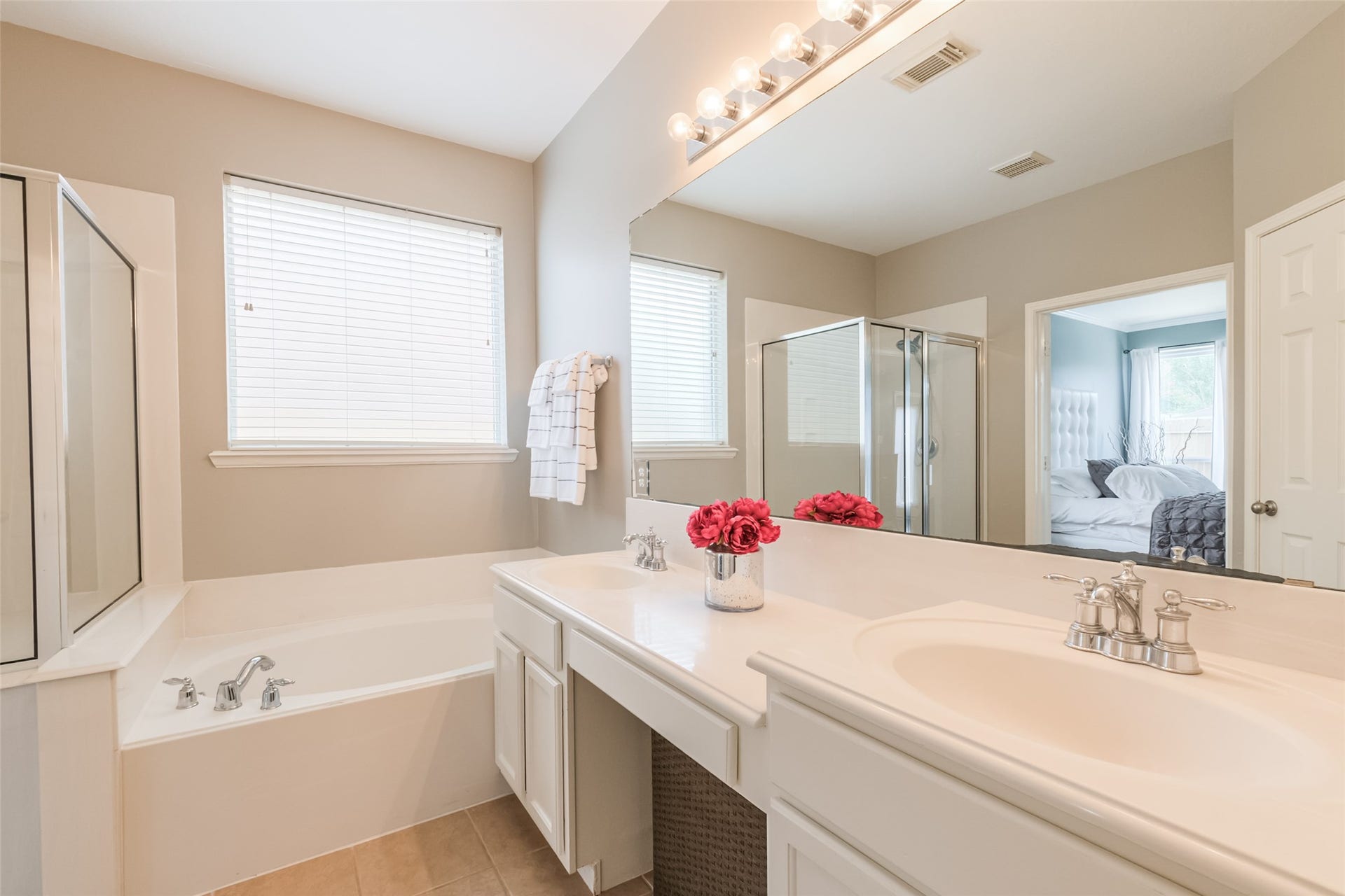 10314 Five Oaks Crossing, Missouri City, TX 77459 This bright bathroom features a spacious vanity with dual sinks, a large mirror with vanity lights, a soaking tub, and a separate walk-in shower. Neutral tones and natural light create a relaxing atmosphere, with a glimpse into the adjoining bedroom.