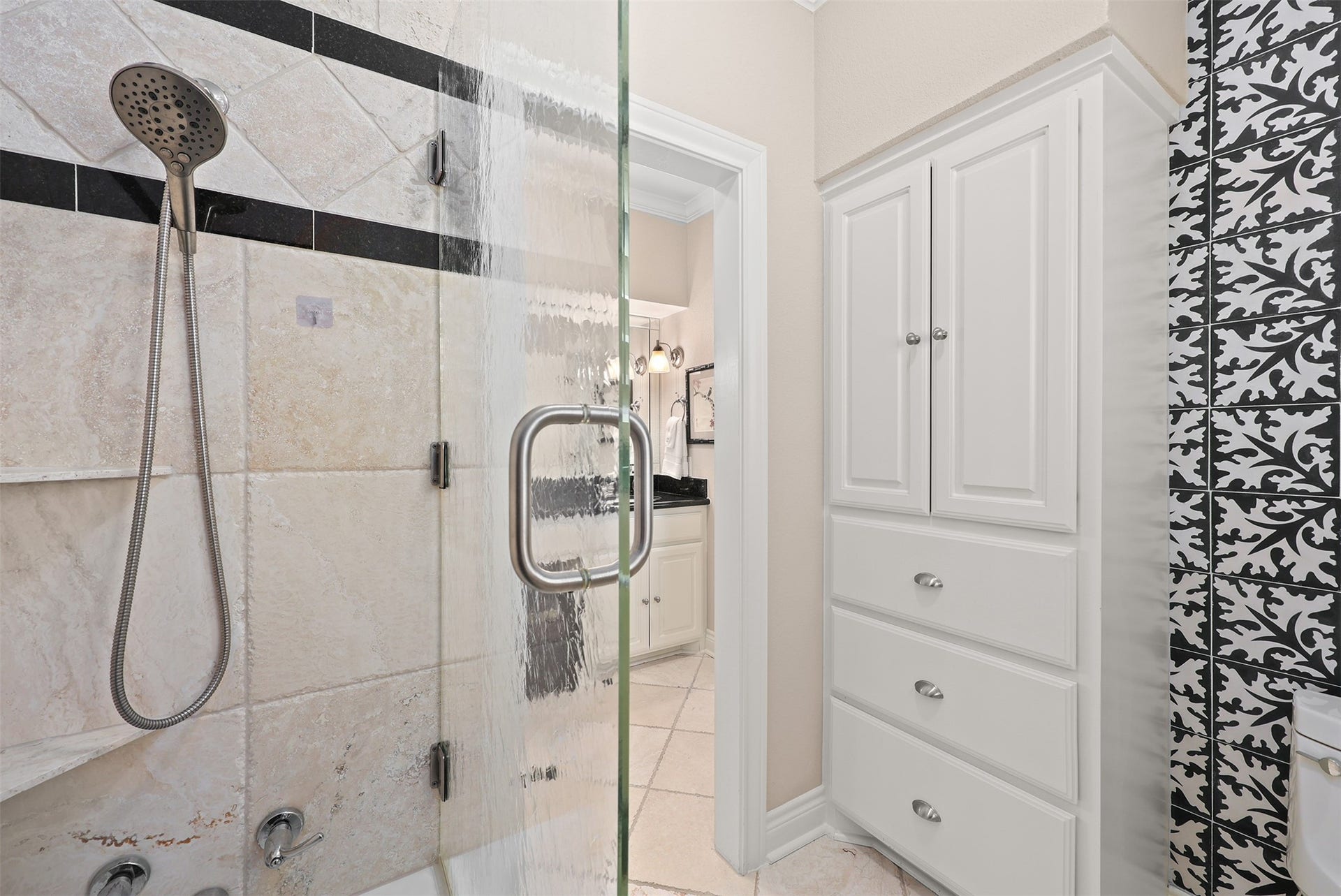 18607 Point Lookout Drive, Nassau Bay, TX 77058 This beautifully designed black-and-white bathroom features abundant custom cabinetry and drawers, a tub/shower combination with tub-to-ceiling tile, and a sleek European-style glass enclosure. Decorative black-and-white patterned tile adds a striking touch of timeless elegance.