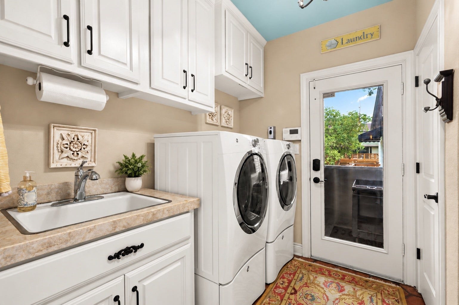 18607 Point Lookout Drive, Nassau Bay, TX 77058 Spacious laundry room featuring abundant storage cabinetry, a utility sink with Taj Mahal quartzite countertop, and a convenient half bath. A glass door leads to the covered exterior elevator/lift, ideally located near the kitchen for easy loading and unloading of groceries. Refrigerator in laundry room conveys with the house.