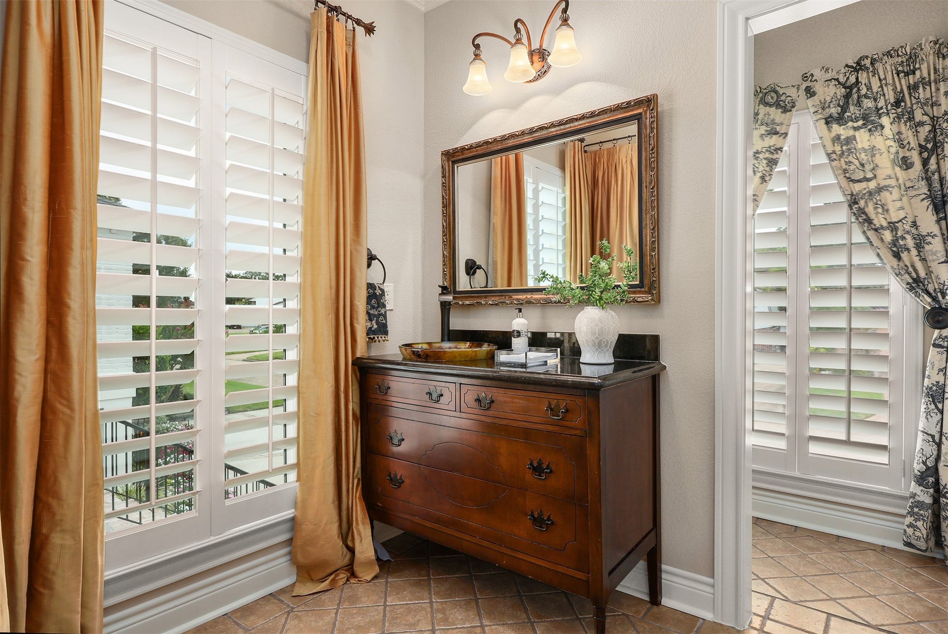 18607 Point Lookout Drive, Nassau Bay, TX 77058 The adjoining full bath to bedroom one features a charming antique furniture-style vanity with a beautiful sink, two windows with plantation shutters, and a separate private toilet area.
