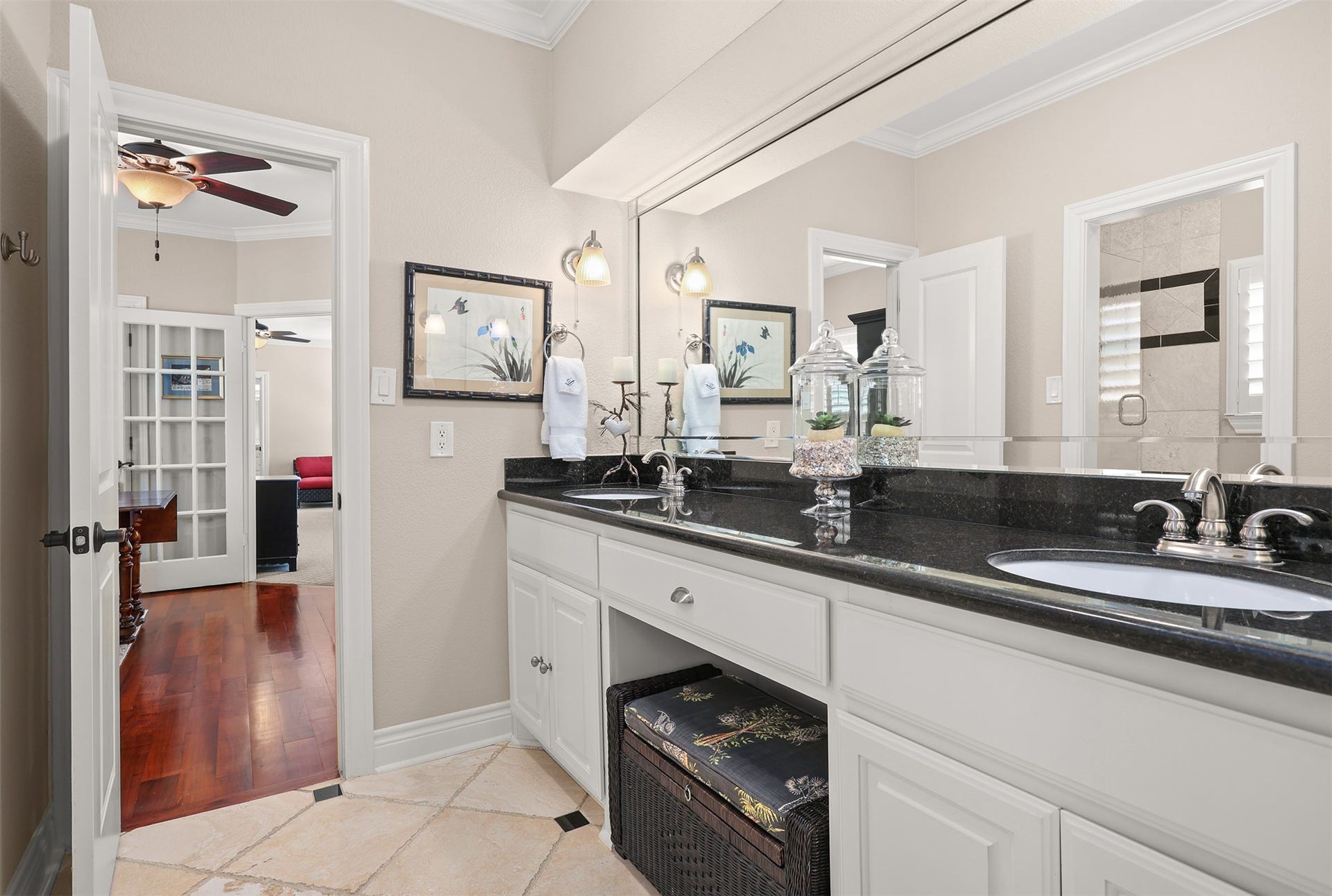 18607 Point Lookout Drive, Nassau Bay, TX 77058 Spacious shared bathroom features beautiful creamy white cabinetry, elegant black granite countertops, double sinks, and an expansive beveled mirror spanning the vanity. Decorative wall sconces provide soft, inviting lighting, while generous counter space and abundant cabinetry offer both comfort and functionality.