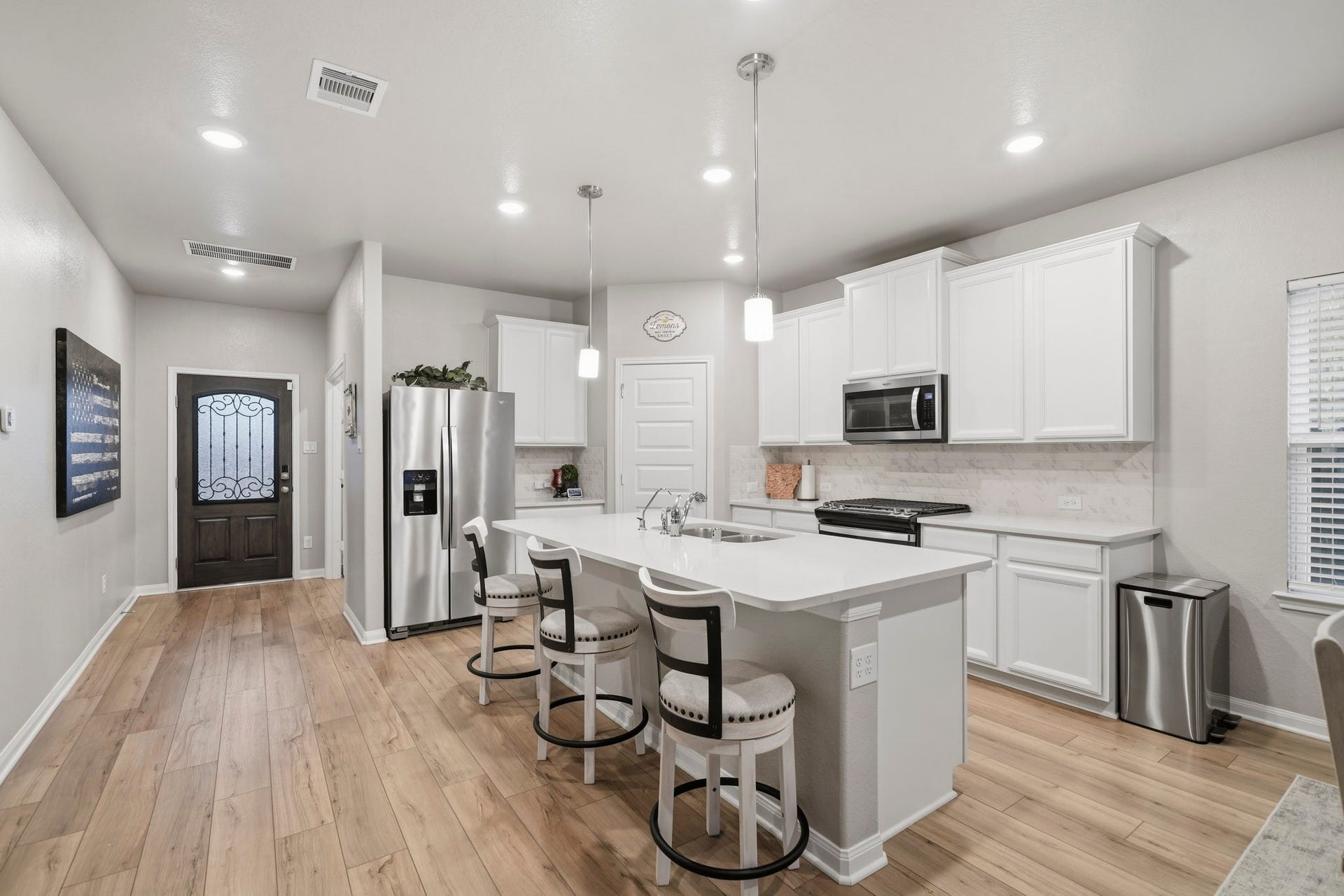 Modern kitchen with sleek white cabinetry, stainless steel appliances, and a spacious island with seating, complemented by elegant lighting and warm