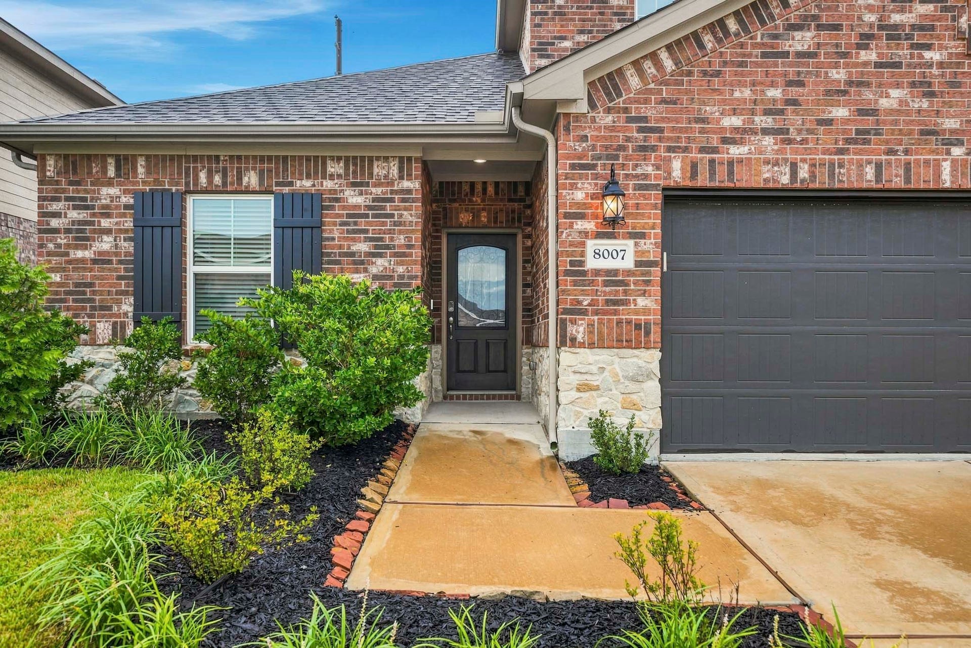 Charming brick and stone exterior with elegant dark accents, a neatly landscaped front yard, and a welcoming entryway.