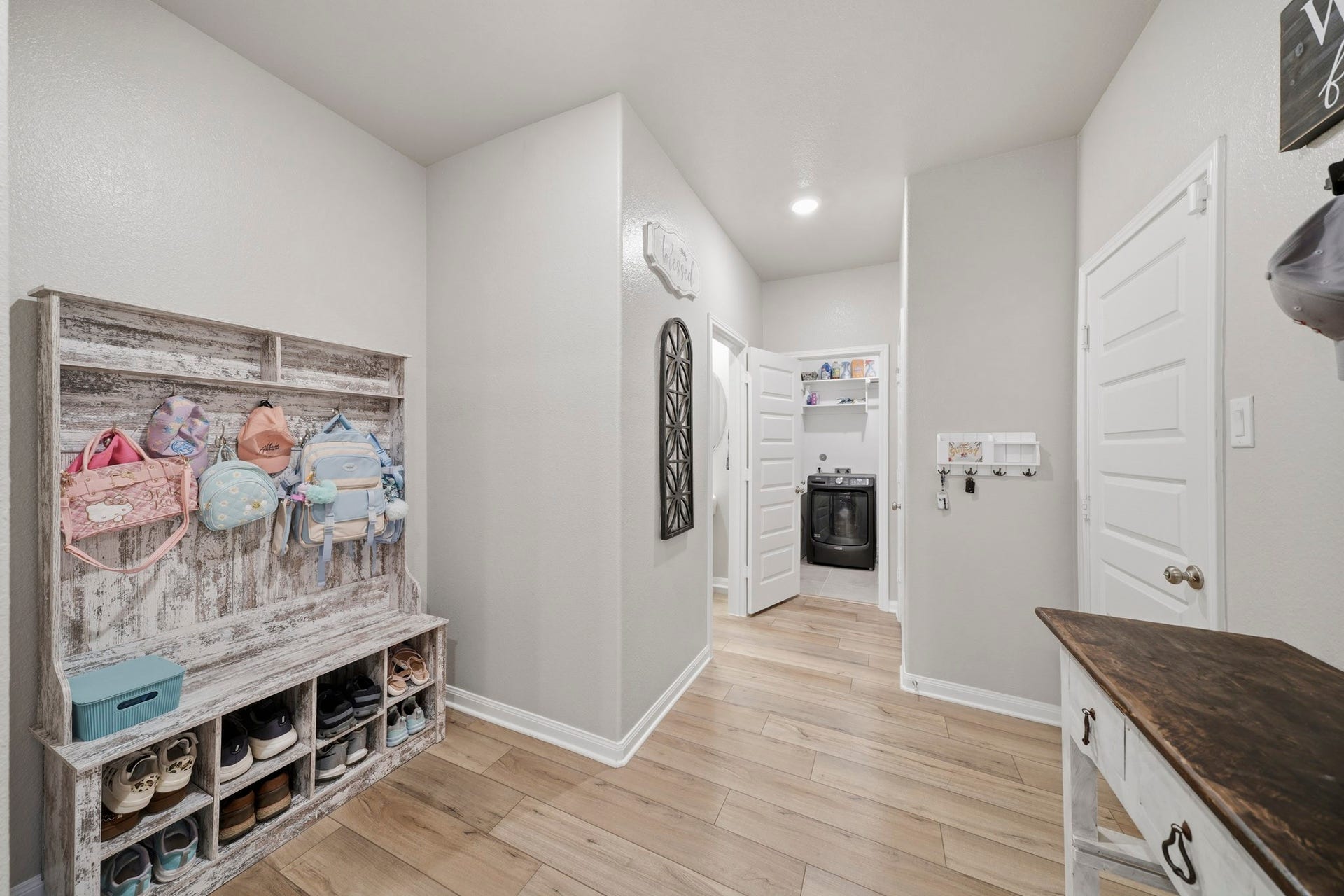 Charming mudroom featuring a rustic shoe storage bench and convenient hooks for bags, leading to a modern laundry room with ample shelving.