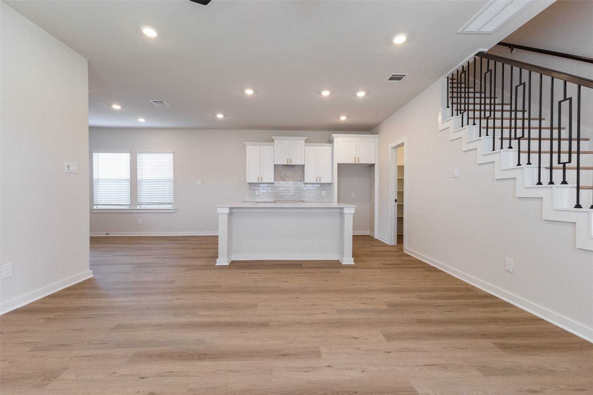 1007 Santee Ct Court, Rosharon, TX 77583 Looking from the living room back toward the kitchen, the quartz-topped island becomes the heart of the home, with space for barstools on one side and prep room on the other. White shaker cabinets reach up high for extra storage, and the staircase and walk-in pantry sit just beyond. The straight sightlines make it easy to keep an eye on the whole main floor while you cook.
