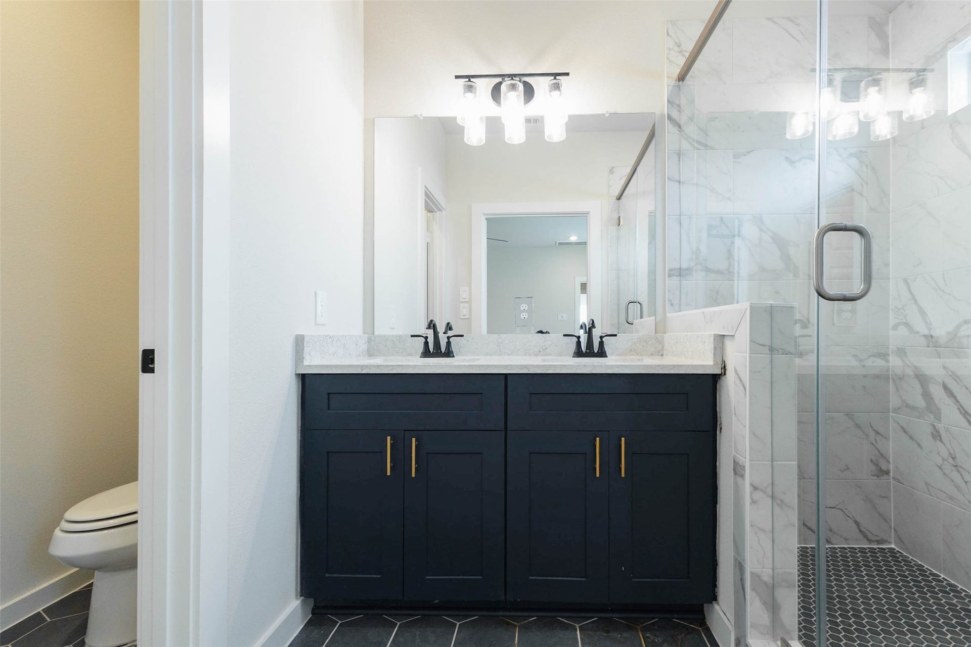 1007 Santee Ct Court, Rosharon, TX 77583 The primary bath is a retreat, with a dual-sink navy vanity, quartz counters, gold pulls and a frameless glass shower wrapped in marble-look tile. A private water closet gives extra privacy, and the stylish light fixture adds a bit of sparkle. Two sinks mean no waiting in the morning, and the dark cabinets against bright tile make it feel like a boutique hotel.