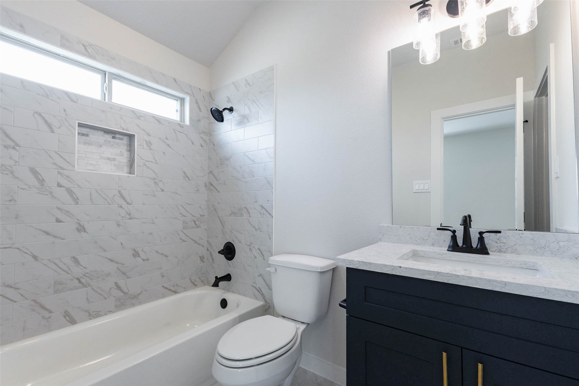 1007 Santee Ct Court, Rosharon, TX 77583 Another full bath has a tub-shower wrapped in marble-look tile with a built-in shelf niche, a high transom window and matte black fixtures. A navy vanity with a quartz top matches the primary bath, giving the home a cohesive, designer feel. A full bathroom serving the extra bedrooms keeps mornings running smoothly and gives guests their own comfortable space.