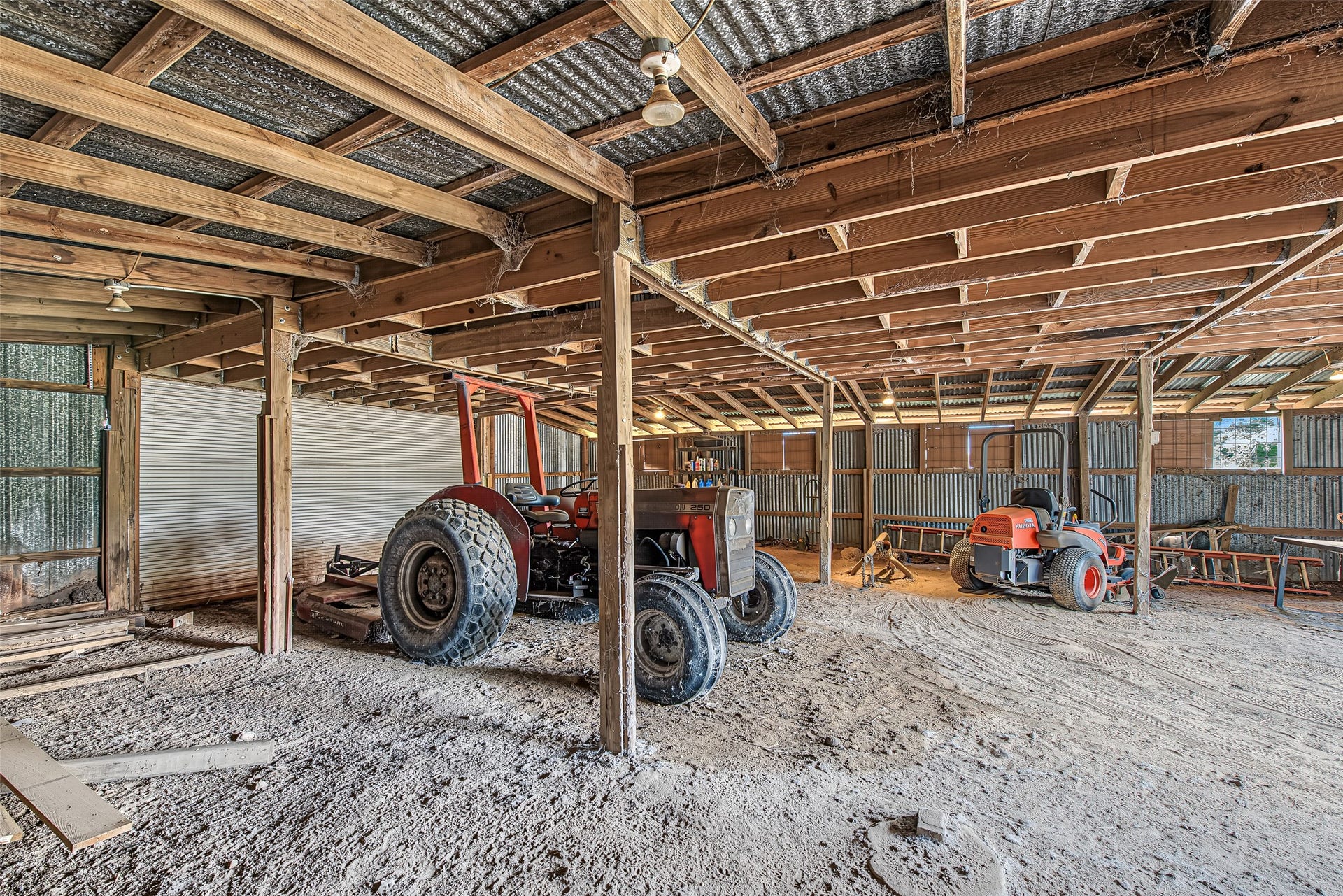 Providing essential protection from the elements, the spacious interior of this barn features heavy-duty exposed post-and-beam timber framing, a sturdy corrugated metal roof structure, and overhead lighting.