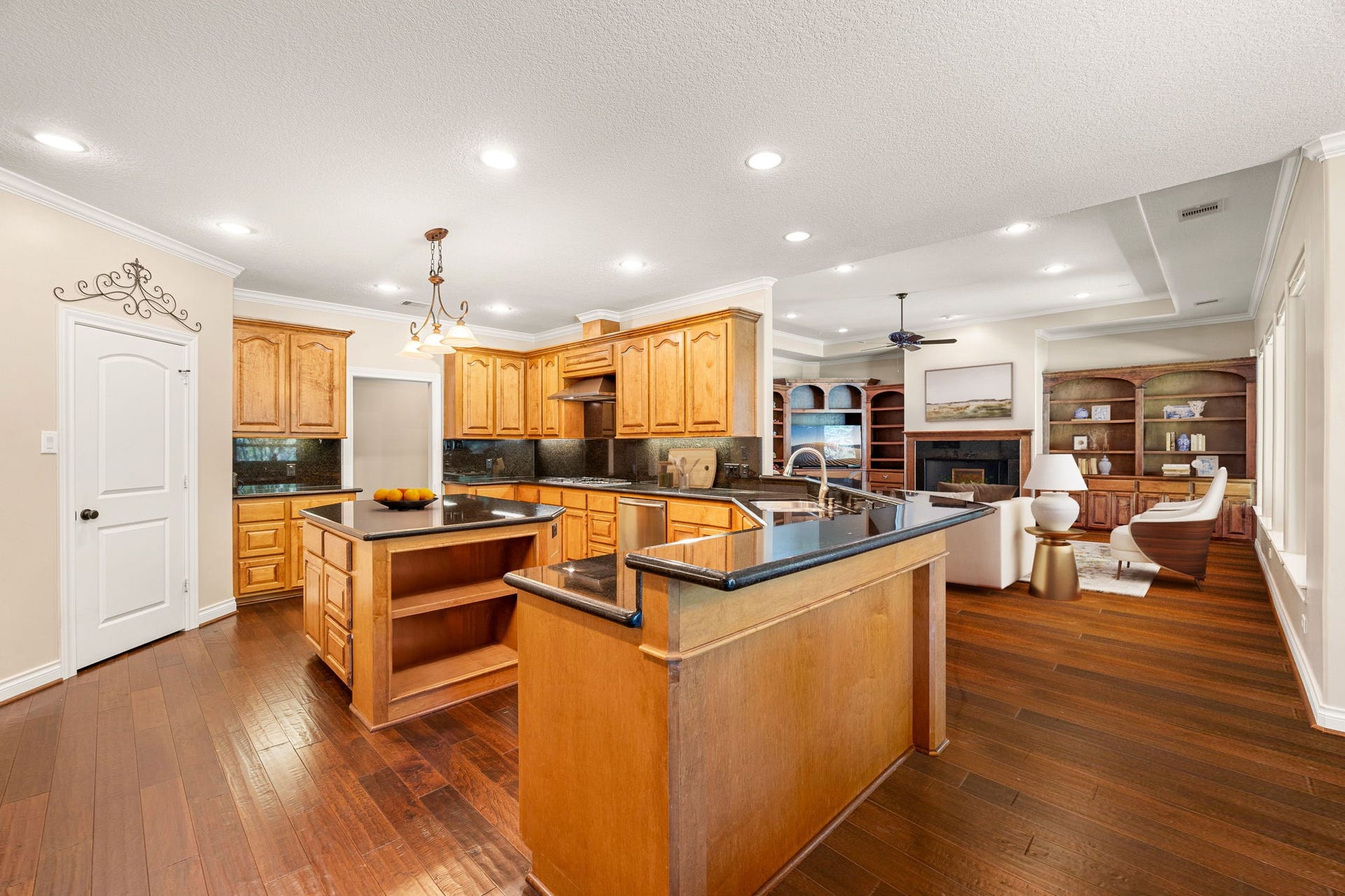 13506 Stagecoach Road, Magnolia, TX 77355 This expansive kitchen blends warmth and functionality with rich wood cabinetry, sleek granite countertops, and a spacious center island perfect for meal prep or gathering. Overlooking the inviting living area, the open layout enhances flow and connection, while recessed lighting and elegant crown molding add a touch of sophistication.