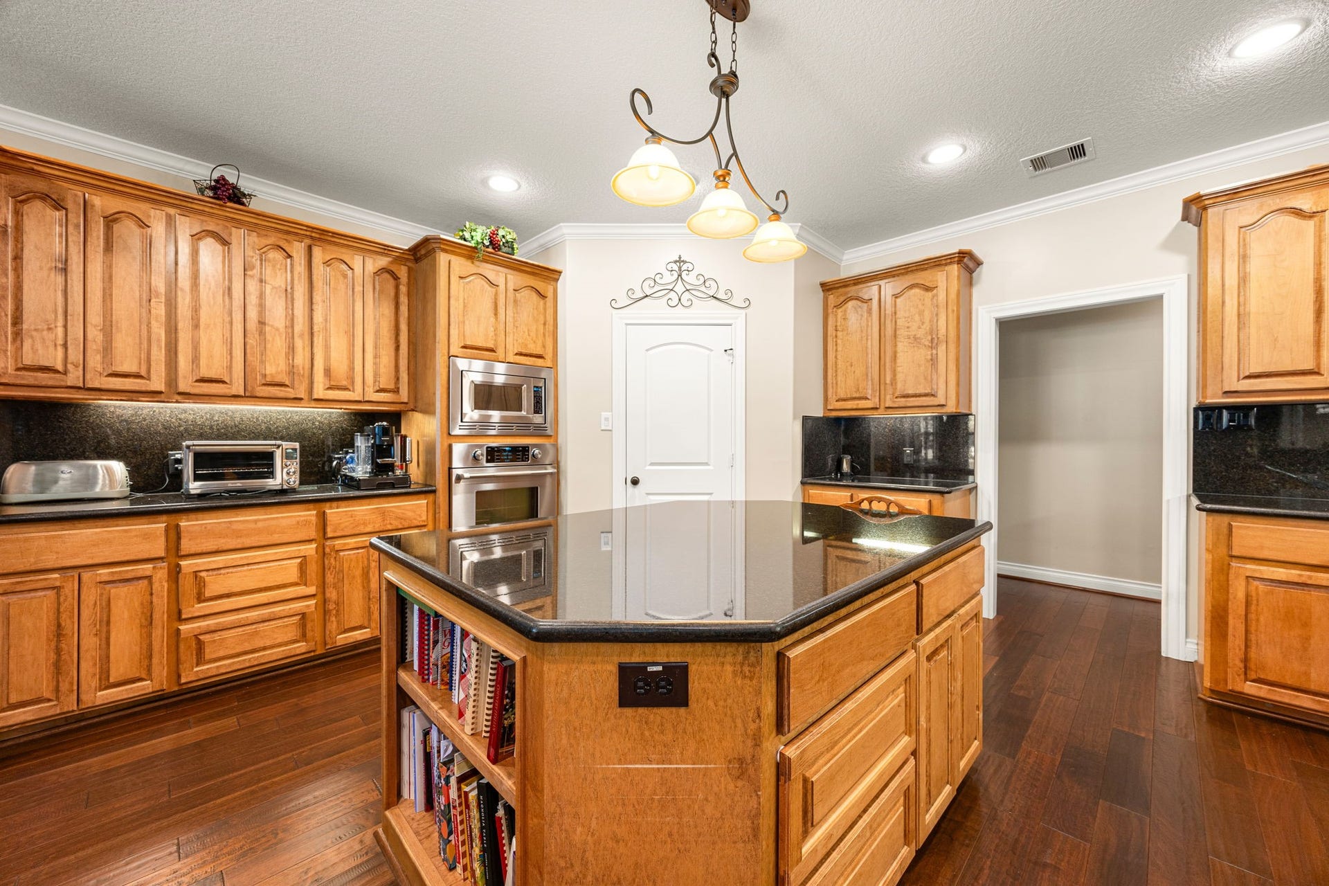 13506 Stagecoach Road, Magnolia, TX 77355 This chefs kitchen offers both elegance and efficiency, showcasing custom wood cabinetry, granite countertops, and a spacious island with built-in shelving. Stainless steel appliances and rich wood flooring complete the space, blending timeless style with everyday functionality.