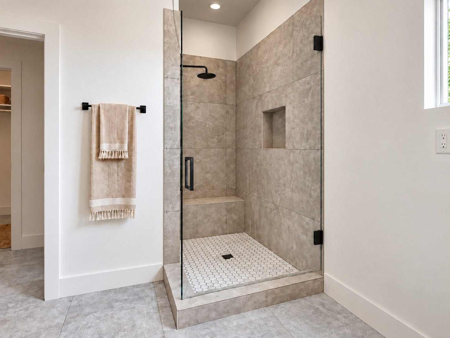 6027 Beall Street, Houston, TX 77091 Experience a beautifully designed walk-in shower featuring elegant floor-to-ceiling textured tile, sleek frameless glass doors, and sophisticated matte black fixtures. A rainfall showerhead provides a spa-inspired experience, while the built-in bench and recessed storage niche offer everyday convenience. The white hexagonal mosaic flooring adds a stylish contrast to the warm neutral tile. These photos have been virtually rendered for visual reference.