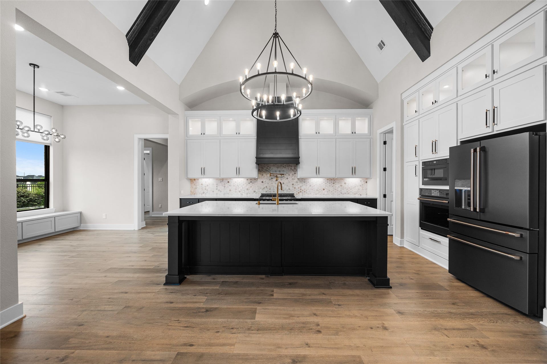 6707 Nimitz Court, Katy, TX 77493 Striking chefs kitchen centered around an oversized island with waterfall-style quartz countertops, contrasting cabinetry, and statement chandelier beneath vaulted ceilings with exposed beams.