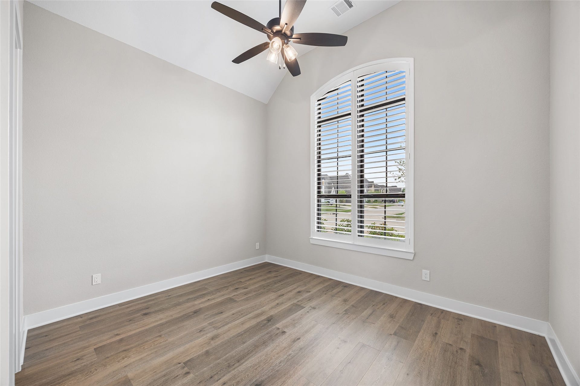 6707 Nimitz Court, Katy, TX 77493 Spacious secondary bedroom with vaulted ceilings, wide-plank flooring, and a large arched window with plantation shutters offering natural light and neighborhood views.