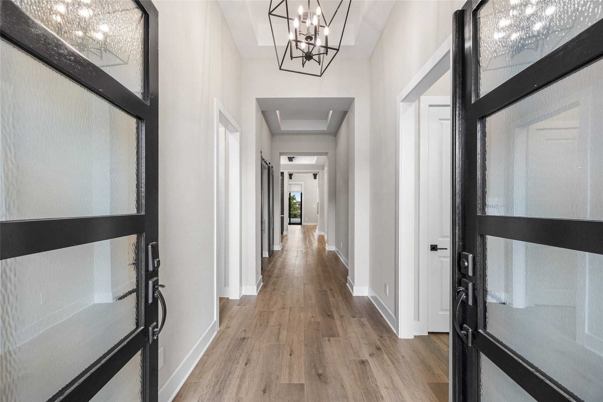 6707 Nimitz Court, Katy, TX 77493 Inviting front entry with double glass doors opens to a long, light-filled hallway featuring high ceilings, wood-look flooring, and a statement chandelier that creates a grand first impression.