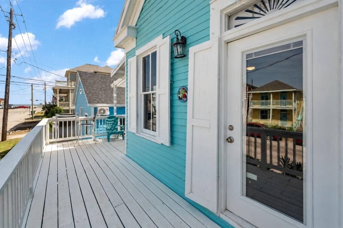 1805 19th Street, Galveston, TX 77550 Second-Floor Deck: Enjoy coastal living from this inviting second-floor deck featuring vibrant turquoise siding, white railings, and outdoor seating. Conveniently accessible from the living area, this charming outdoor space offers views toward the Gulf and a relaxing setting to enjoy the coastal breeze, just approximately 1 blocks from the beach!