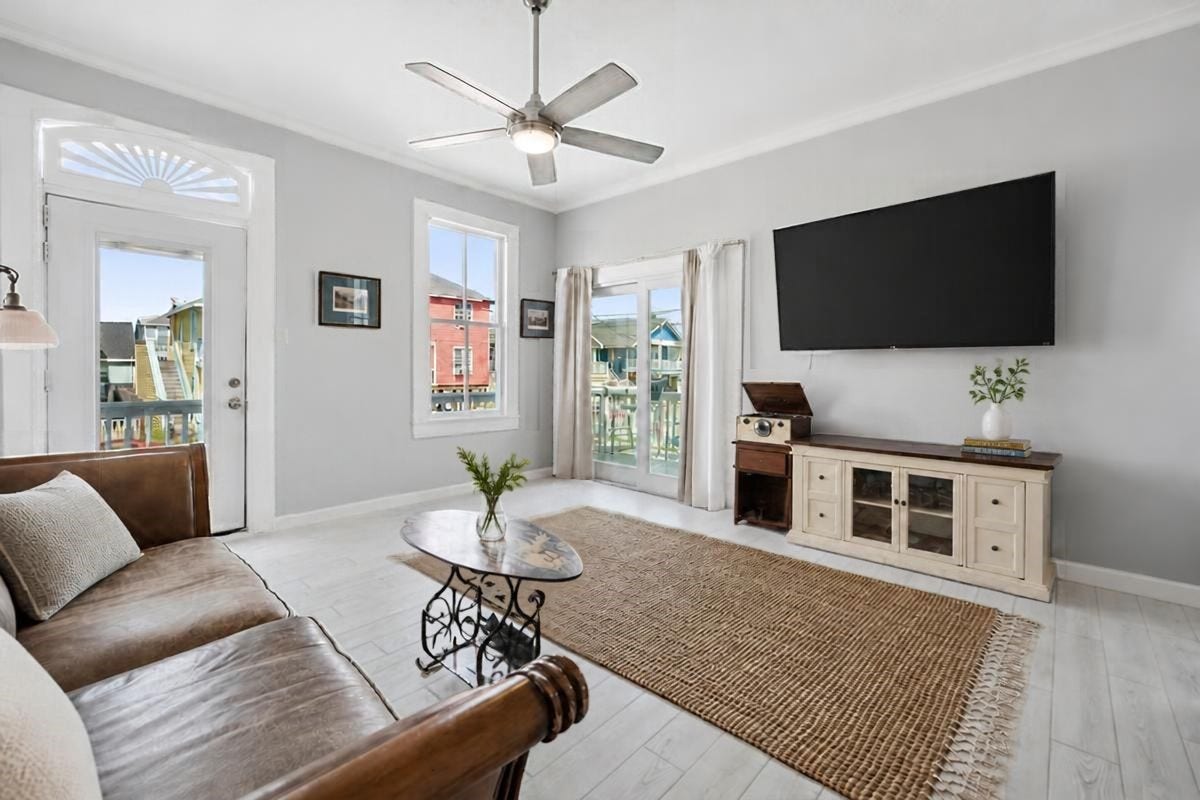 1805 19th Street, Galveston, TX 77550 Second-Floor Living Area: Bright and inviting second-floor living area featuring abundant natural light, neutral coastal tones, and a ceiling fan. French doors open to the outdoor upper deck, creating a seamless connection between indoor and outdoor living. A welcoming space for relaxing or entertaining after a day at the beach!