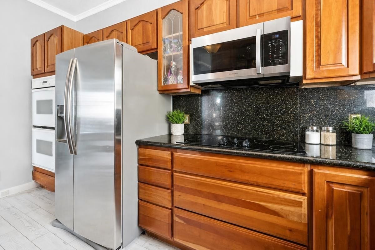 1805 19th Street, Galveston, TX 77550 Additional view of the well-appointed second-floor kitchen, featuring rich wood cabinetry, sleek black granite countertops and backsplash, stainless steel appliances, a smooth-top electric cooktop, built-in microwave, and double ovens. With plenty of storage and convenient meal-preparation space, this inviting kitchen is ready for everything from quick beach-day breakfasts to memorable dinners with family and vacation guests!
