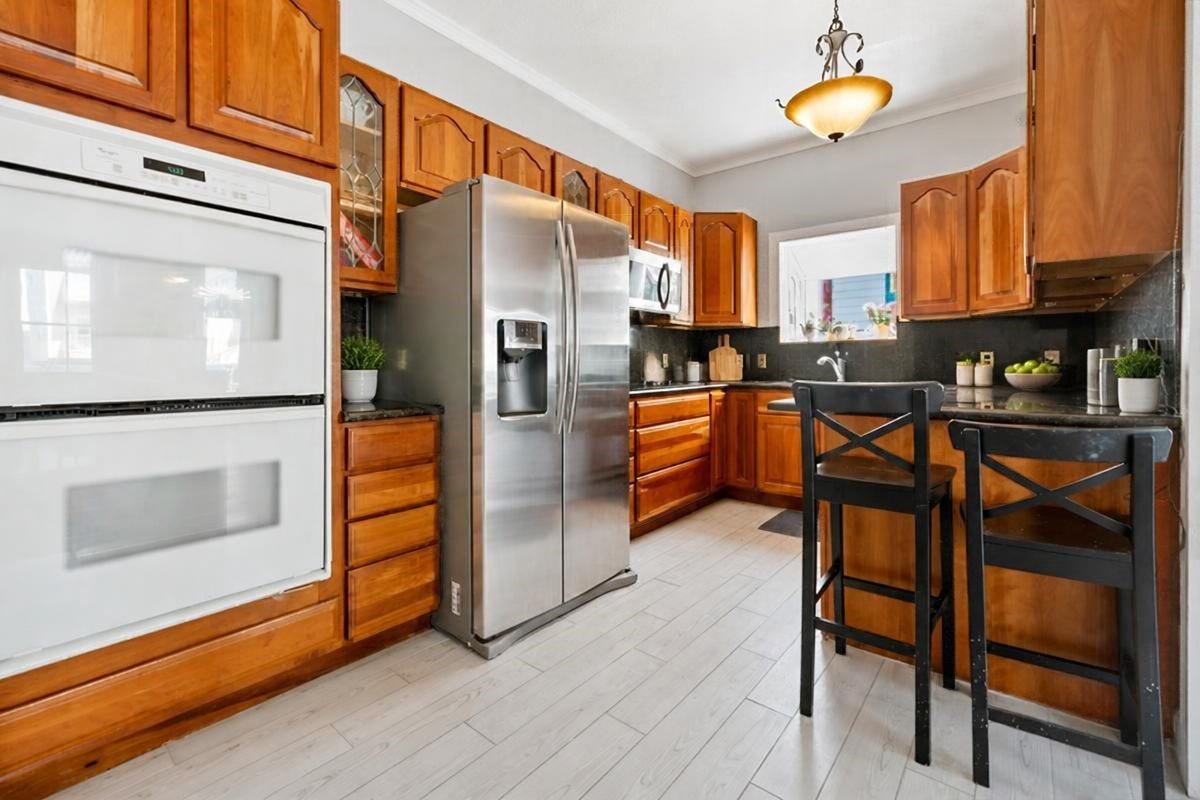 1805 19th Street, Galveston, TX 77550 Second-Floor Kitchen: Welcome to the inviting second-floor kitchen, featuring warm wood cabinetry, generous counter space, a breakfast bar with seating for two, stainless steel refrigerator, built-in double ovens, and wood-look tile flooring. A charming space for preparing meals, gathering with family and friends, and enjoying the relaxed Galveston Island lifestyle after a day at the beach!