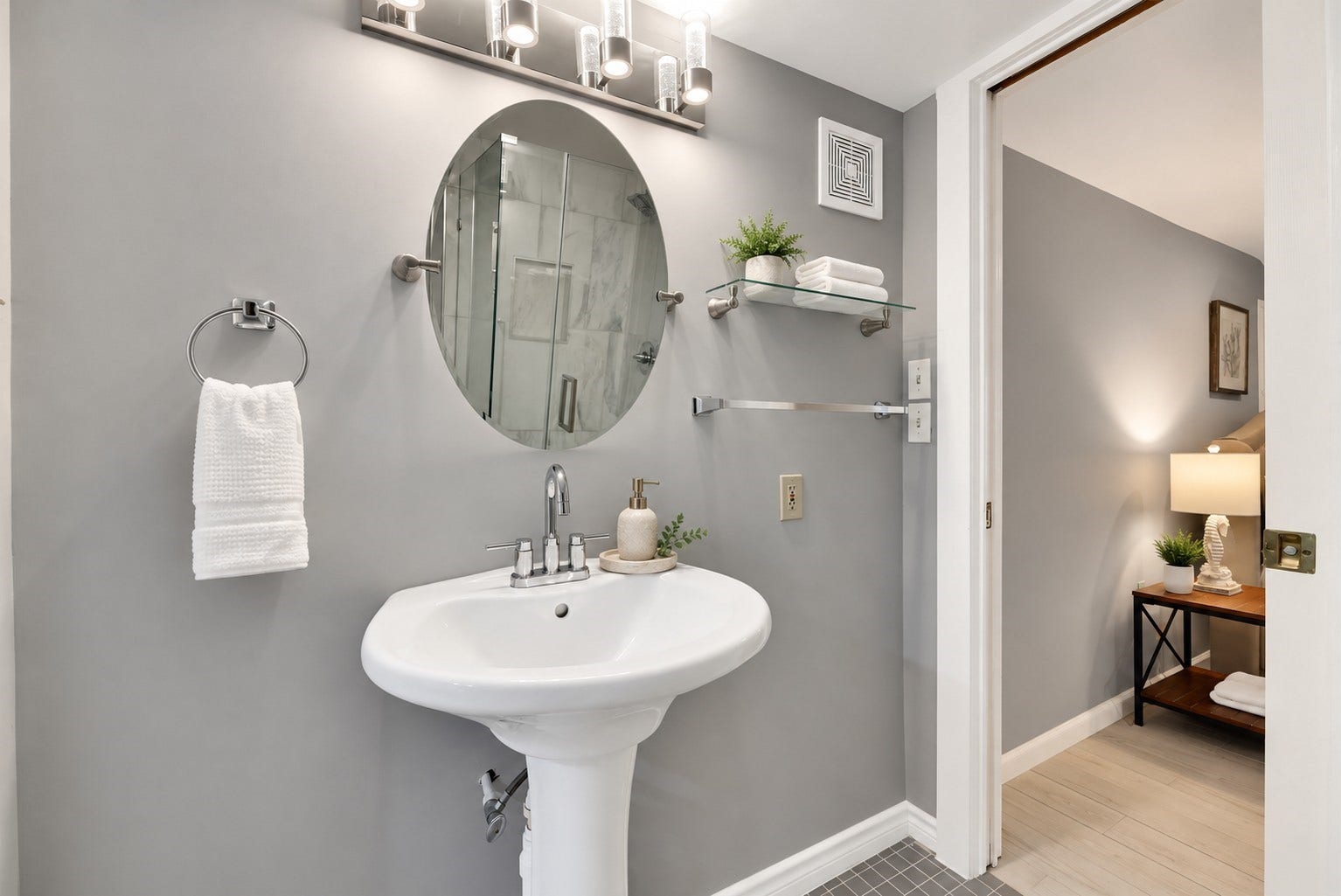 1805 19th Street, Galveston, TX 77550 Additional view of the updated first-floor Jack-and-Jill bathroom shared by Bedrooms 1 and 2. Features a pedestal sink, stylish oval mirror, modern vanity lighting, contemporary fixtures, and neutral gray finishes, creating a clean and inviting coastal feel.