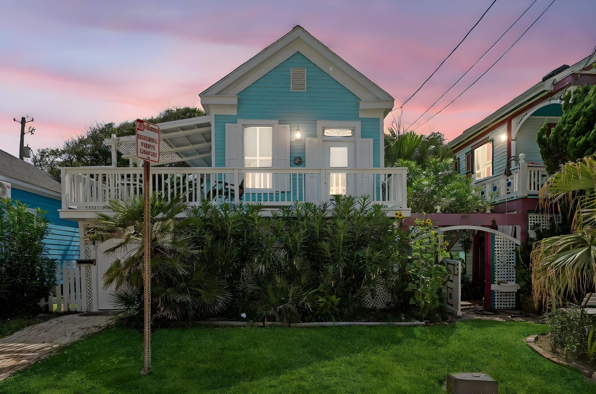 1805 19th Street, Galveston, TX 77550 Twilight view of this charming coastal cottage, featuring an elevated front porch, tropical landscaping, and inviting exterior lighting in a prime Galveston location approximately a block and a half from the beach.