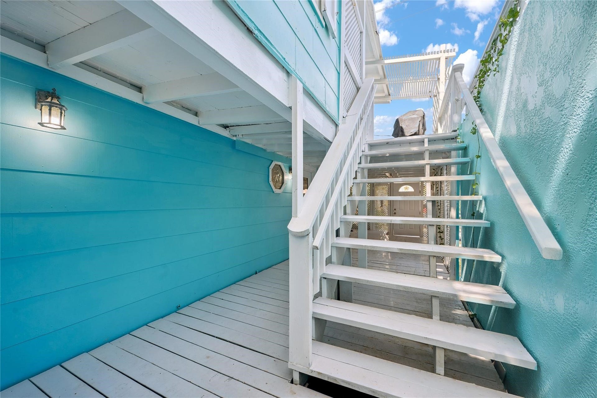 1805 19th Street, Galveston, TX 77550 Exterior Staircase to Second Floor Upper Deck: This inviting exterior staircase, featuring crisp white wooden steps and railings, vibrant turquoise siding, and wall-mounted lighting provides convenient access to the second-floor deck, perfect for enjoying the relaxed beachside lifestyle.