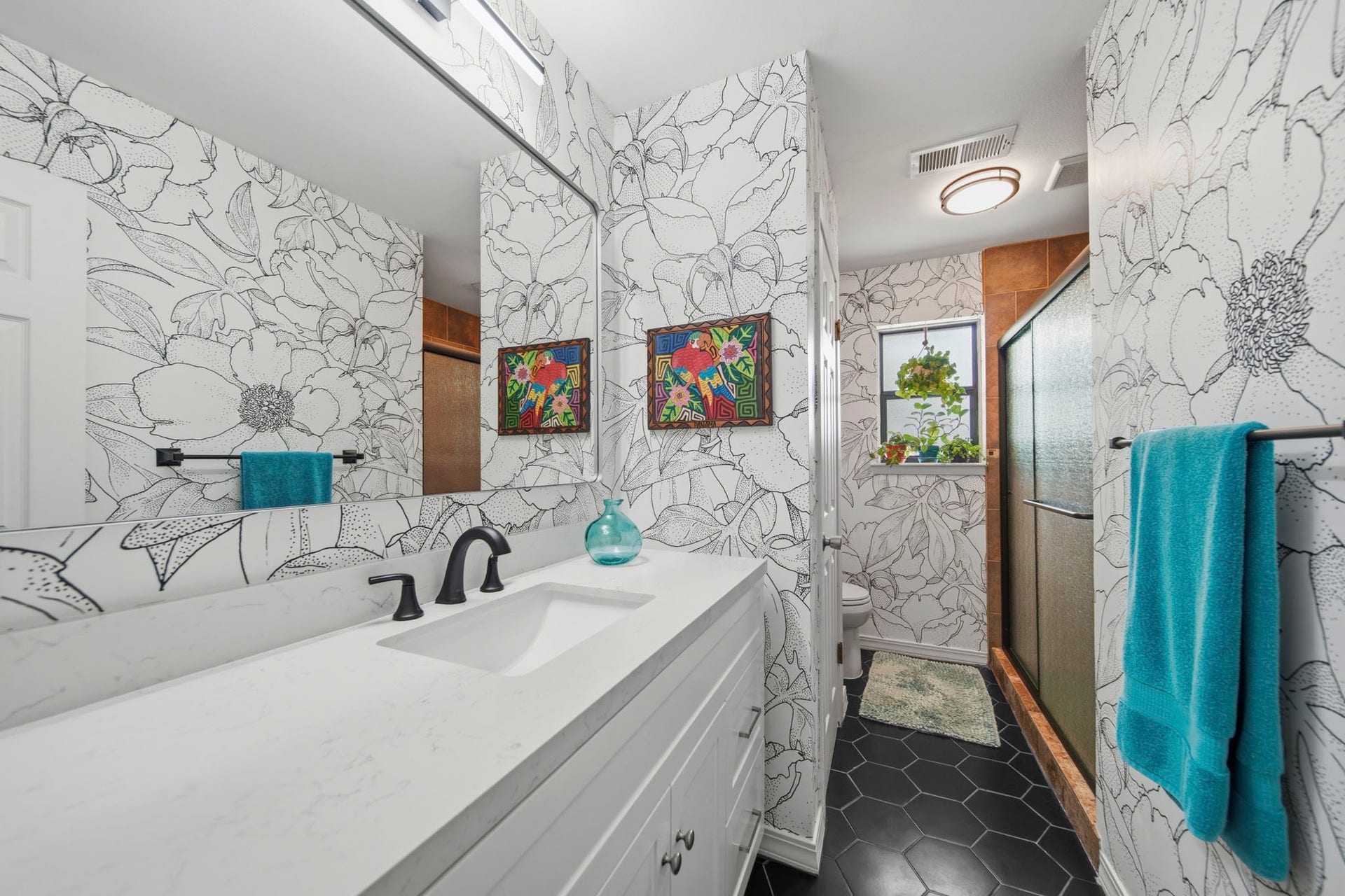 This beautifully upgraded secondary bathroom blends timeless design with modern style, featuring a sleek quartz vanity, designer floral wallpaper, matte black fixtures, and contemporary hex tile flooring. A spacious glass-enclosed shower and fresh, sophisticated finishes create a bright, inviting space that guests and family alike will enjoy!