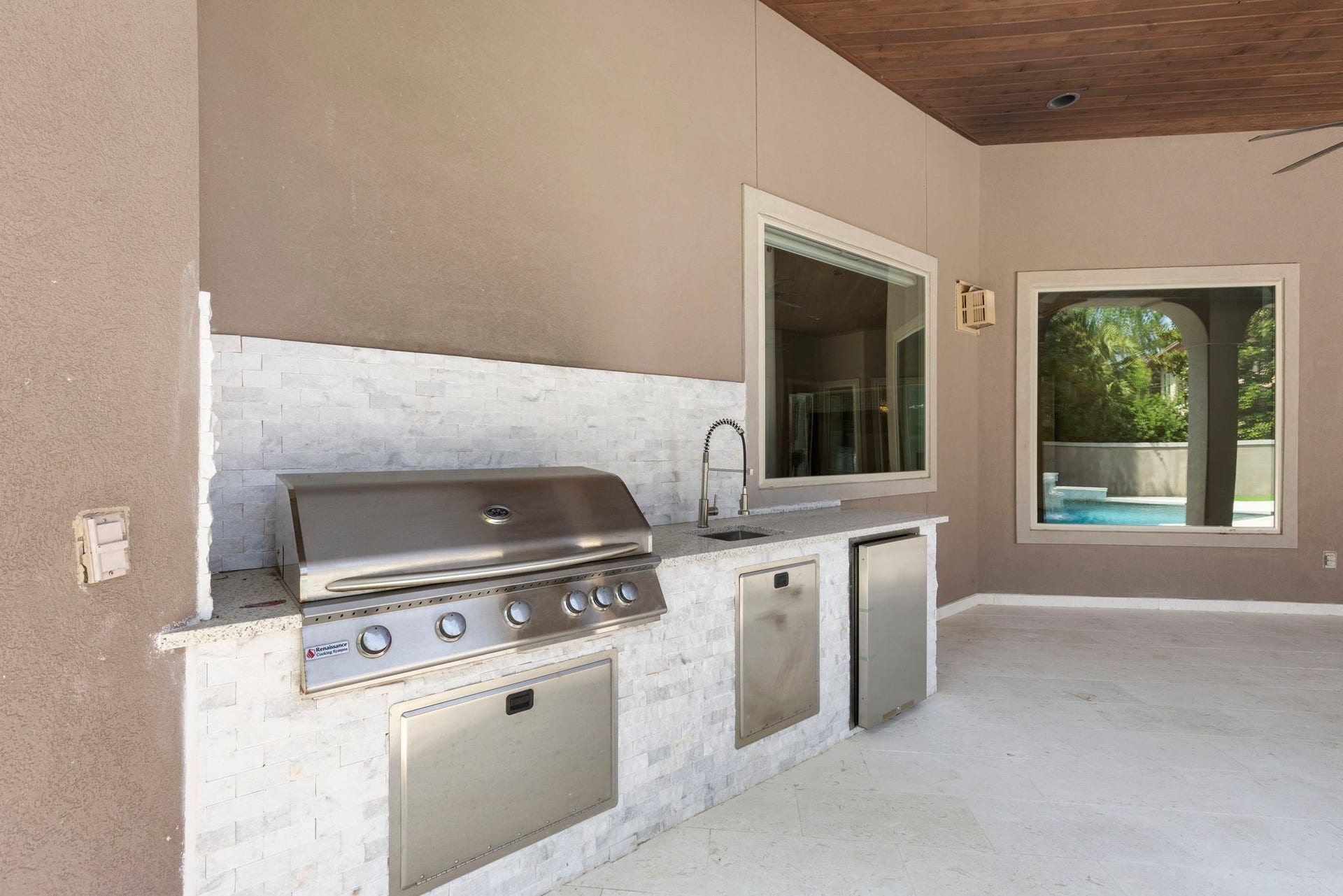 47 Hunnewell Way, The Woodlands, TX 77382 Showcasing a new look all its own, the summer kitchen highlights a gas grill, wet sink, storage and mini fridge with updated stacked stone base, backsplash and counter.