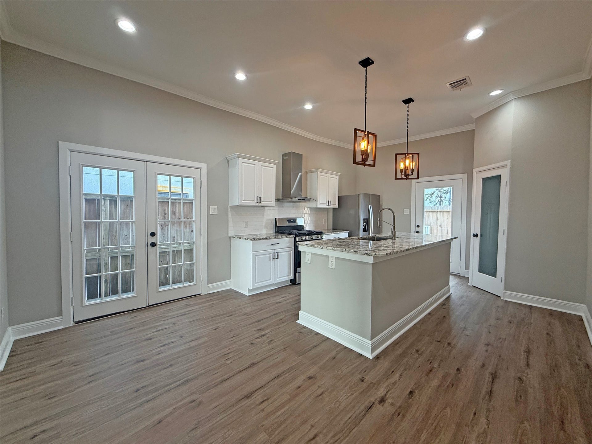 1517 COLORADO Street, Houston, TX 77007 Open-concept kitchen features white cabinetry, granite countertops, stainless steel appliances, and stylish pendant lighting. French doors off the dining area and a separate exterior door near the kitchen provide convenient outdoor access.