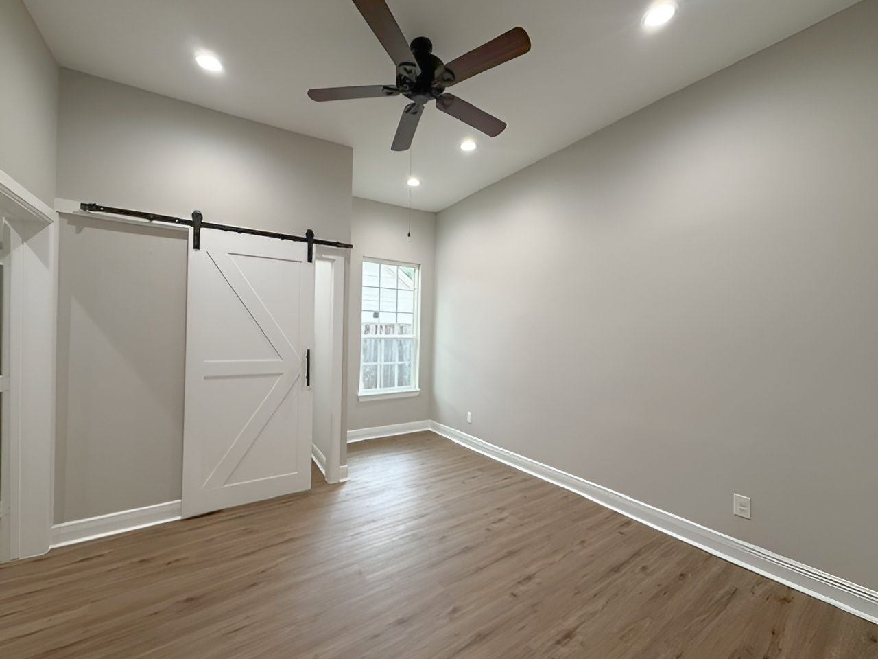1517 COLORADO Street, Houston, TX 77007 Spacious primary bedroom features high ceilings, recessed lighting, a ceiling fan, and a charming sitting area nestled beside the window. A sliding barn door adds a distinctive touch.