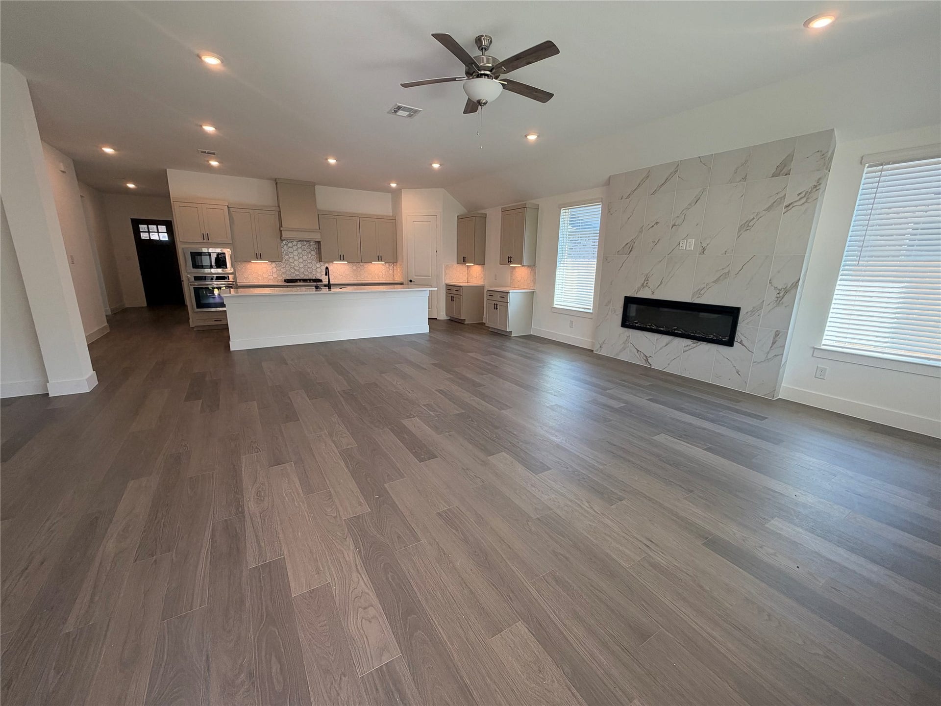 3428 Summercrisp Hollow Lane, Pearland, TX 77581 Spacious open-concept living area featuring sleek hardwood floors, a modern kitchen with a large island, and a stylish fireplace set against a chic tiled wall.