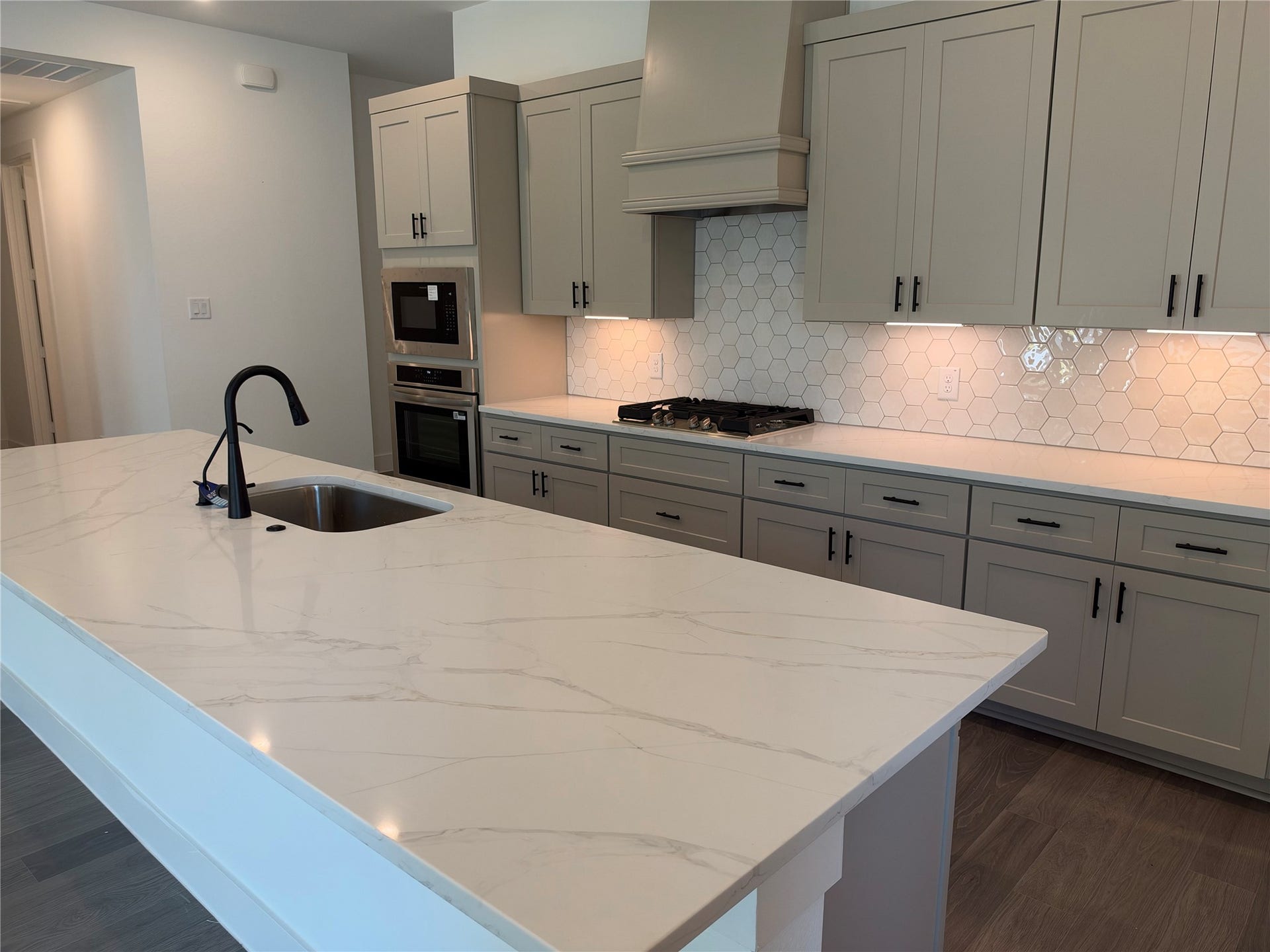 3428 Summercrisp Hollow Lane, Pearland, TX 77581 Modern kitchen featuring sleek gray cabinetry, a spacious marble island with a built-in sink, and a stylish hexagonal tile backsplash, perfect for culinary enthusiasts.