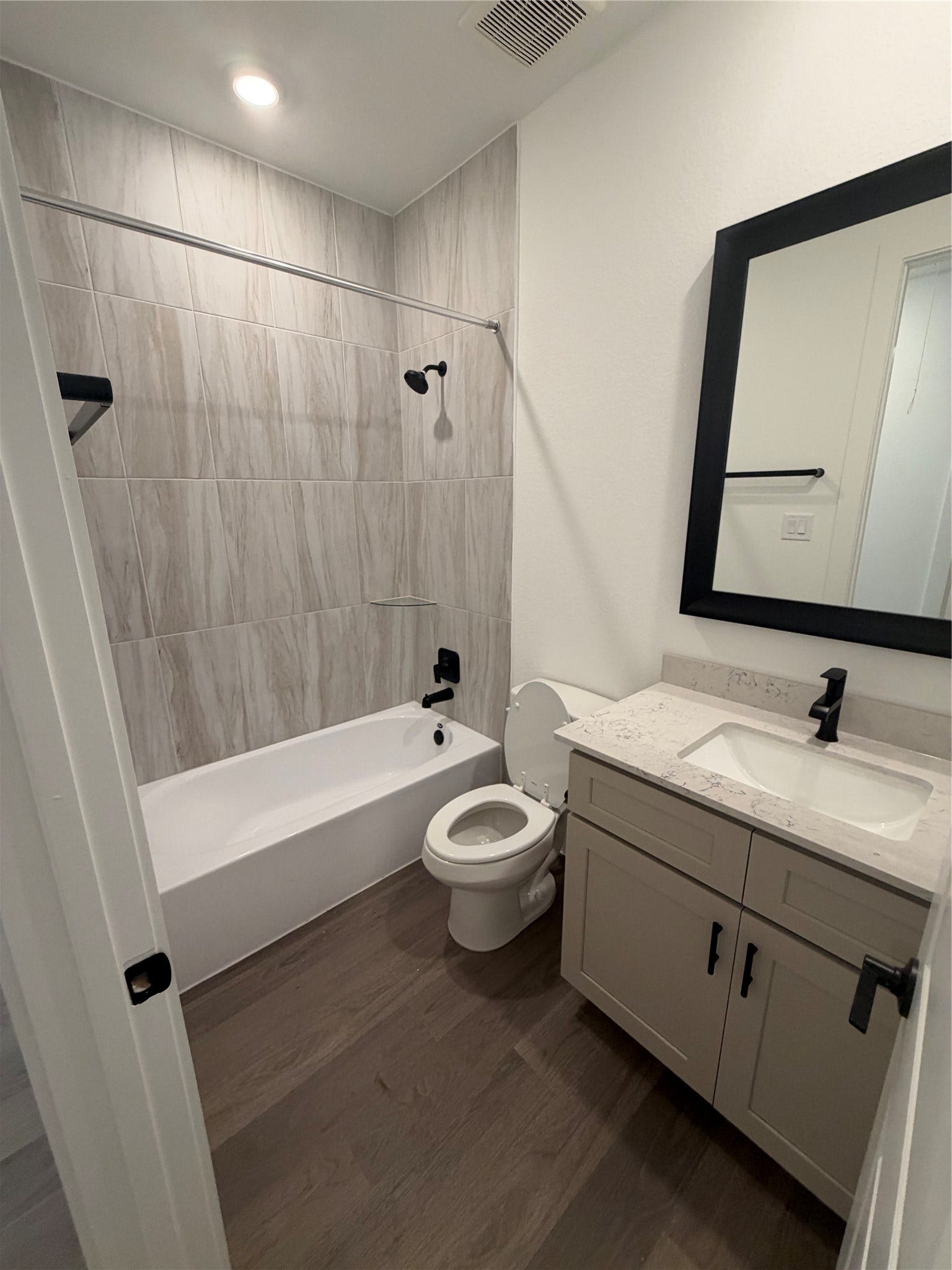 3428 Summercrisp Hollow Lane, Pearland, TX 77581 Modern bathroom featuring sleek wood flooring, a stylish vanity with a marble style countertop, and a tub-shower combo with elegant tile surround.