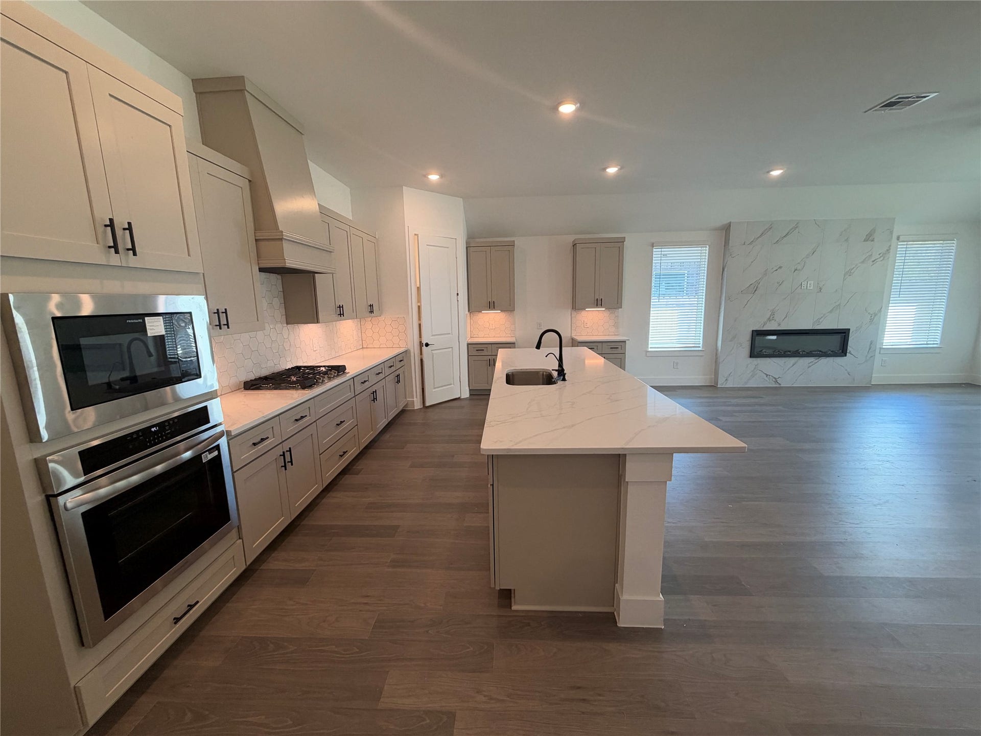 3428 Summercrisp Hollow Lane, Pearland, TX 77581 Spacious modern kitchen with sleek cabinetry, stainless steel appliances, and a large island, seamlessly flowing into an open living area featuring a stylish fireplace.