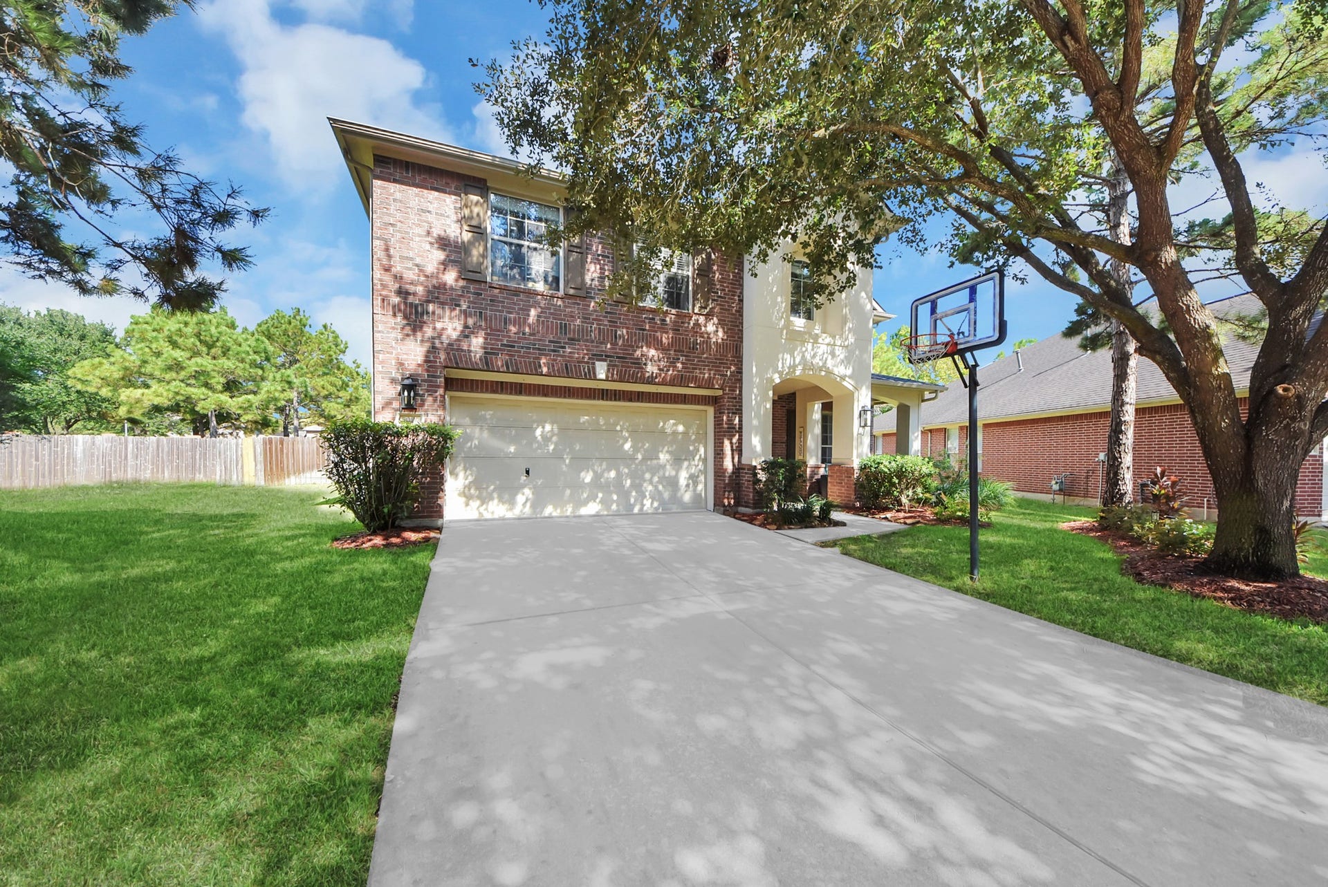 This home offers a classic two-story brick and stucco exterior, mature shade trees, and a spacious driveway with a basketball goal.