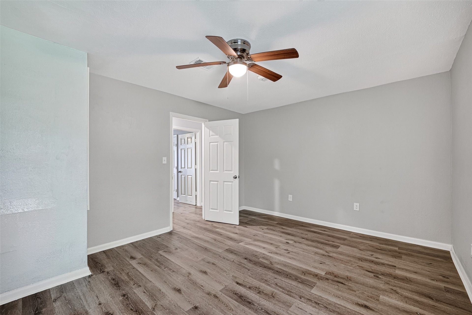 3408 Palm Avenue, Texas City, TX 77590 This room features neutral gray walls and wood-look flooring, complemented by a ceiling fan. The space is bright and open with a door leading to the hallway.