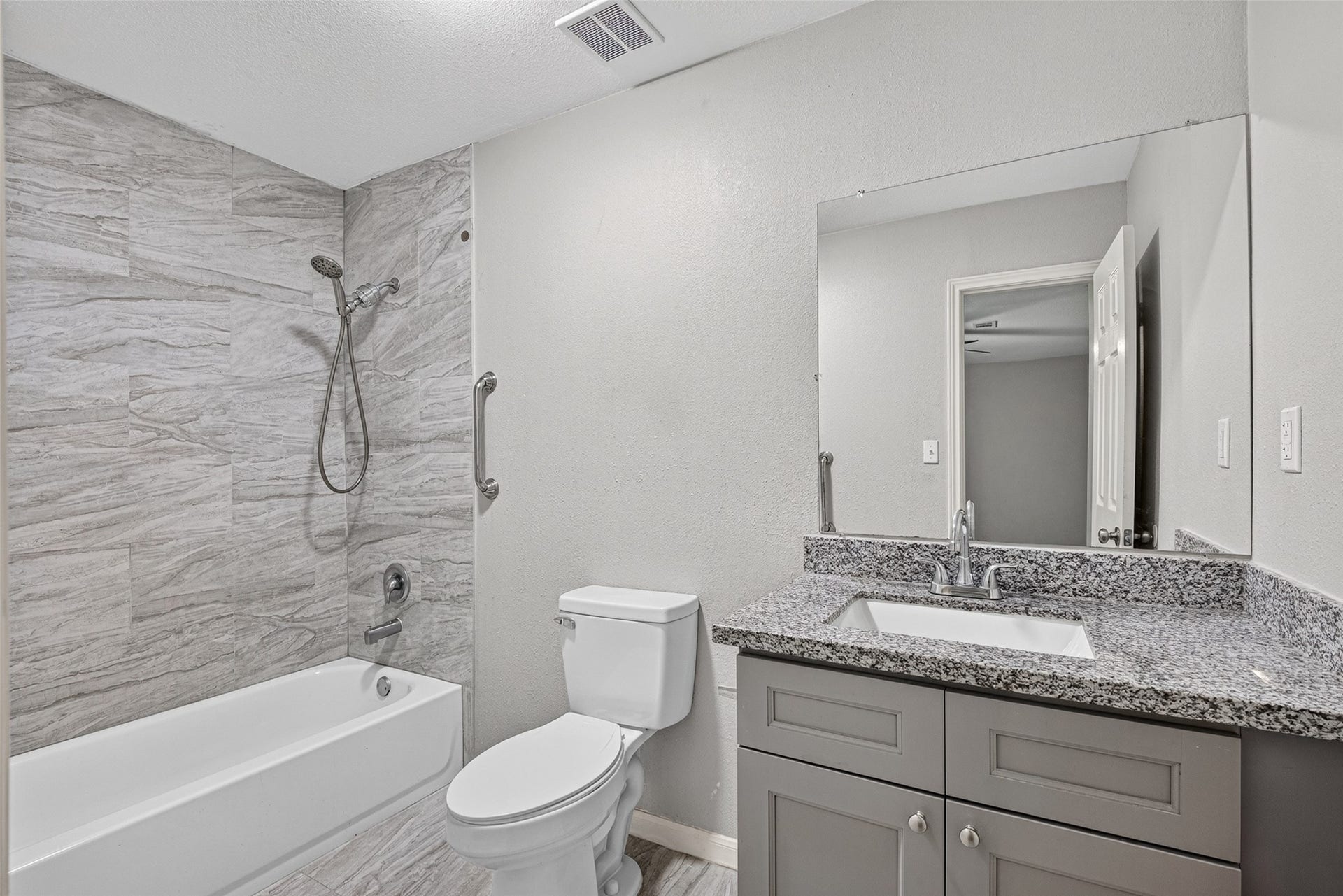 3408 Palm Avenue, Texas City, TX 77590 This bathroom features a modern design with gray tones, showcasing a granite countertop vanity, a large mirror, and a sleek bathtub with tiled walls. Perfect for a contemporary home.