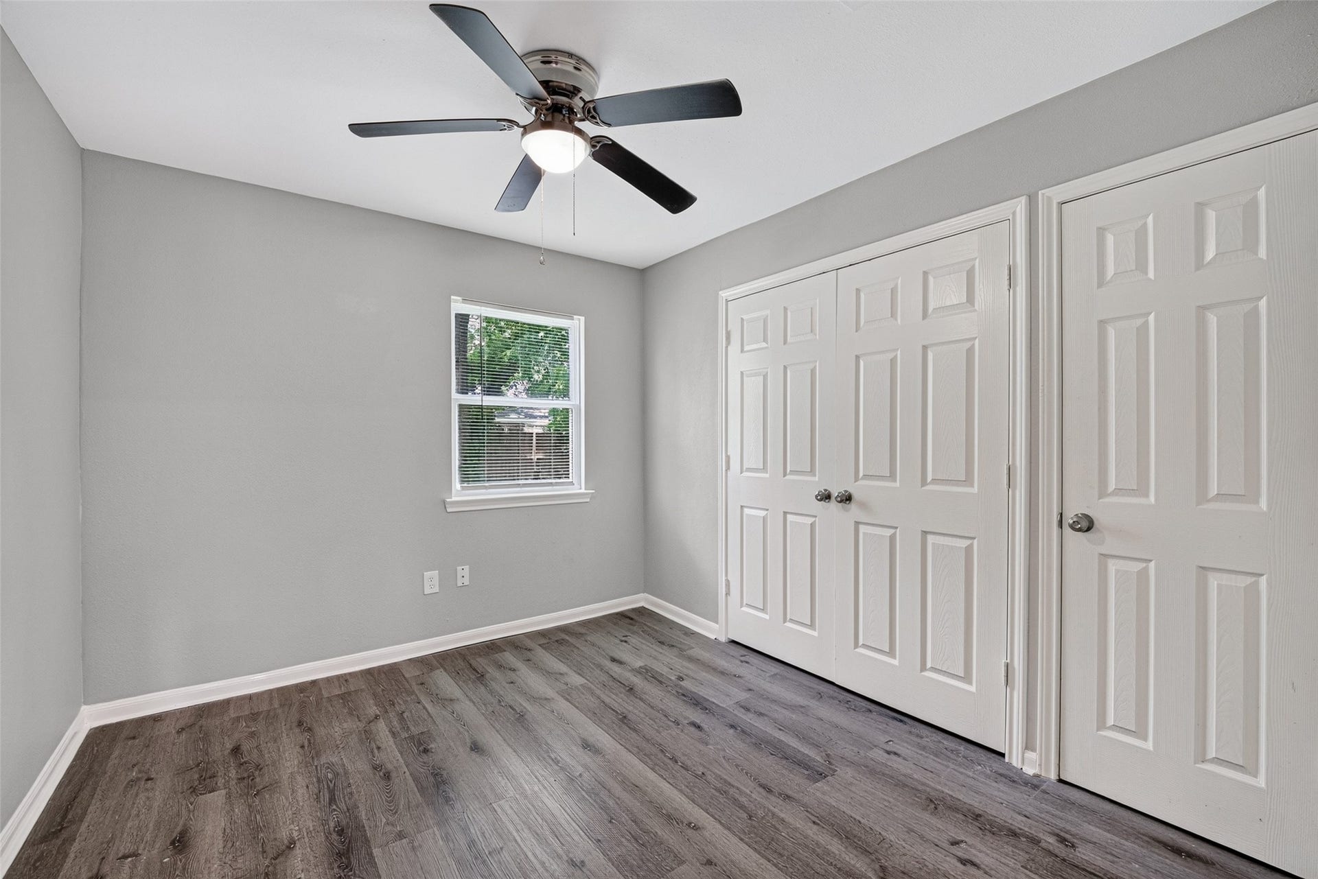 3408 Palm Avenue, Texas City, TX 77590 This room features fresh gray walls, dark wood flooring, a ceiling fan, a window for natural light, and double closets with white doors, offering ample storage.