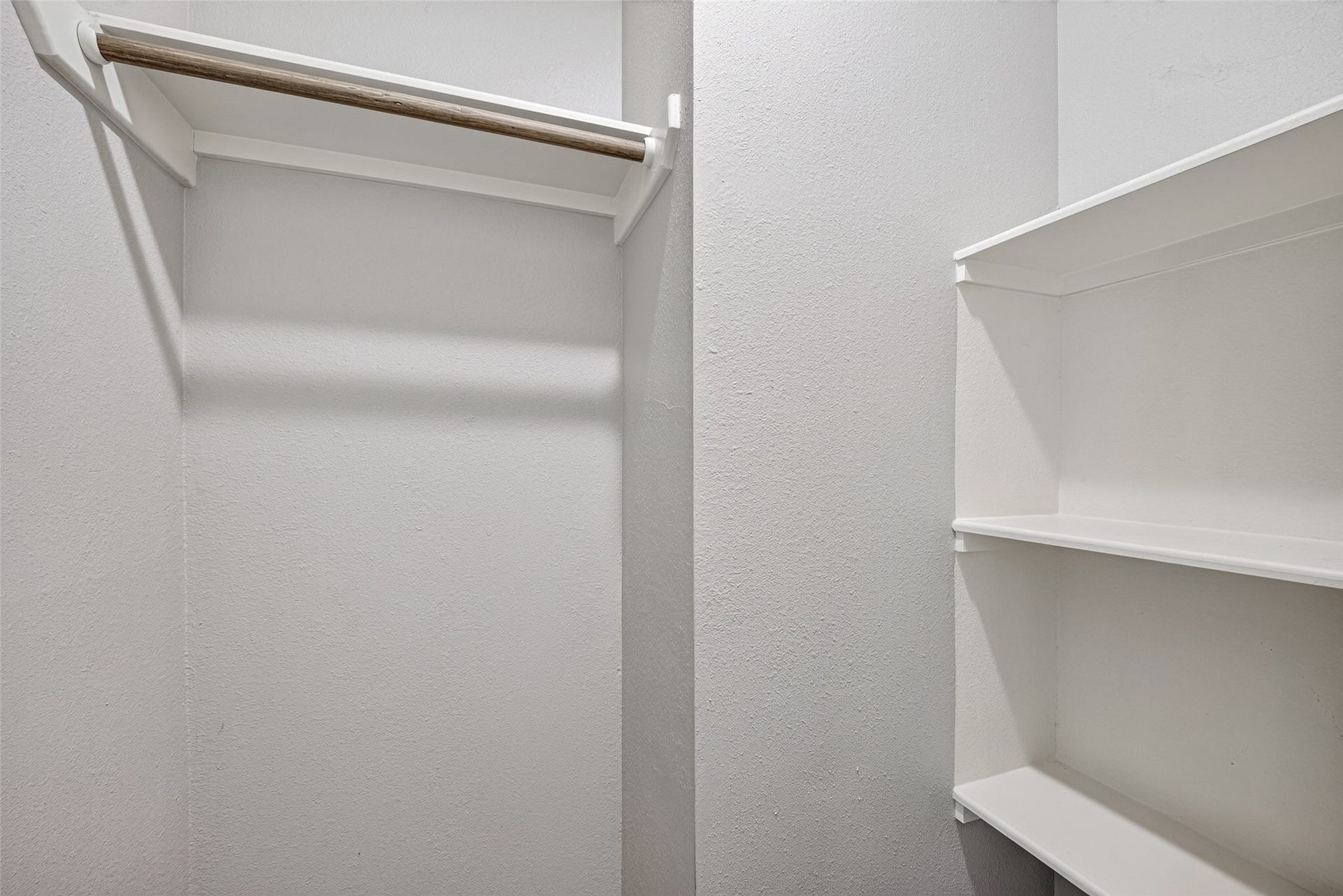 3408 Palm Avenue, Texas City, TX 77590 This photo shows a small walk-in closet with white walls, featuring a wooden hanging rod on the left and built-in shelving on the right, offering practical storage options.