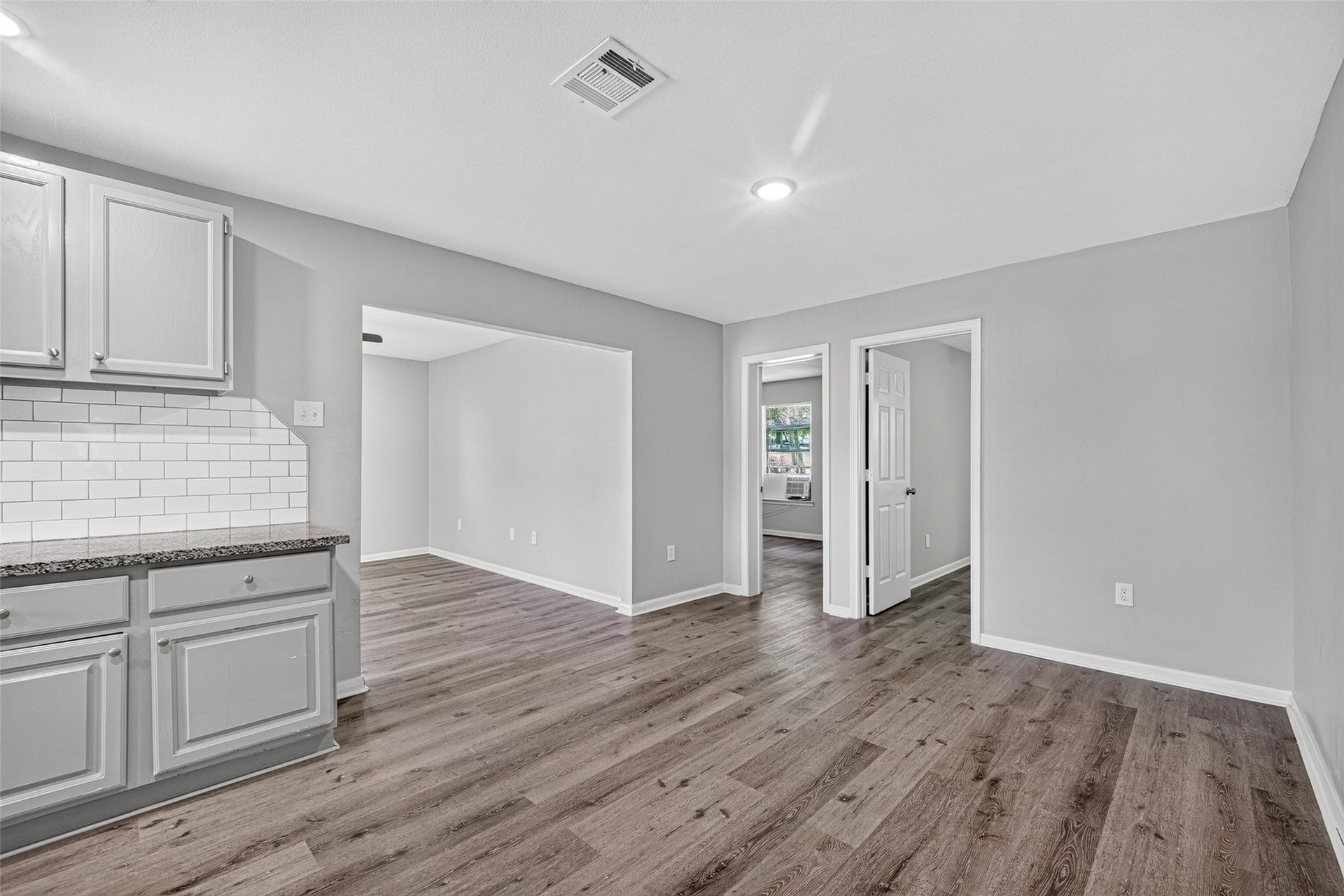 3408 Palm Avenue, Texas City, TX 77590 This photo shows a bright, open-concept living space with modern gray cabinets, white subway tile backsplash, and dark wood flooring. Two doorways lead to adjacent rooms, offering a spacious and versatile layout.