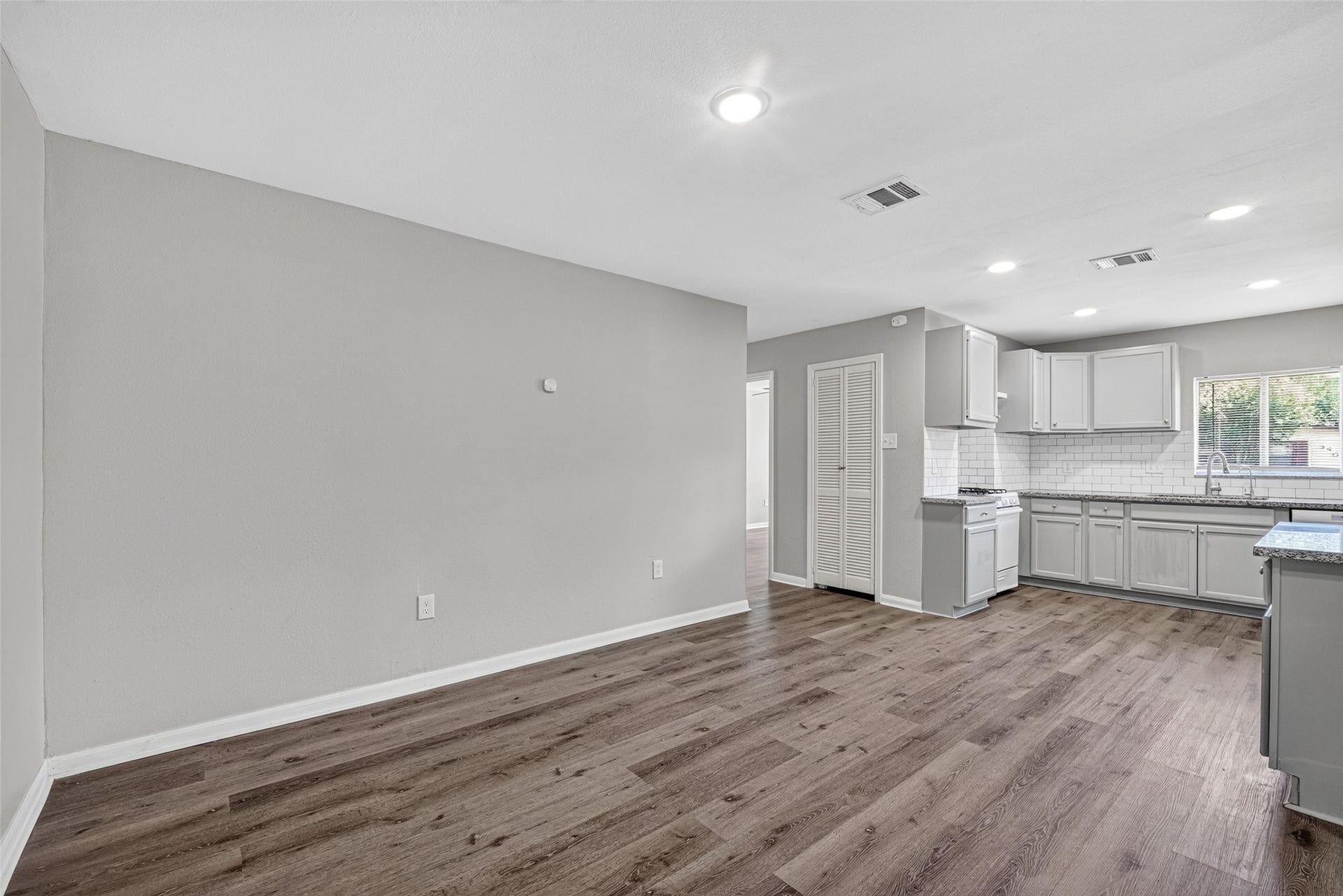 3408 Palm Avenue, Texas City, TX 77590 Discover a sleek, open-plan kitchen and living area with light gray walls, recessed lighting, and elegant wood-look flooring. The kitchen boasts white cabinets, a subway tile backsplash, and a window bathing the space in natural light.