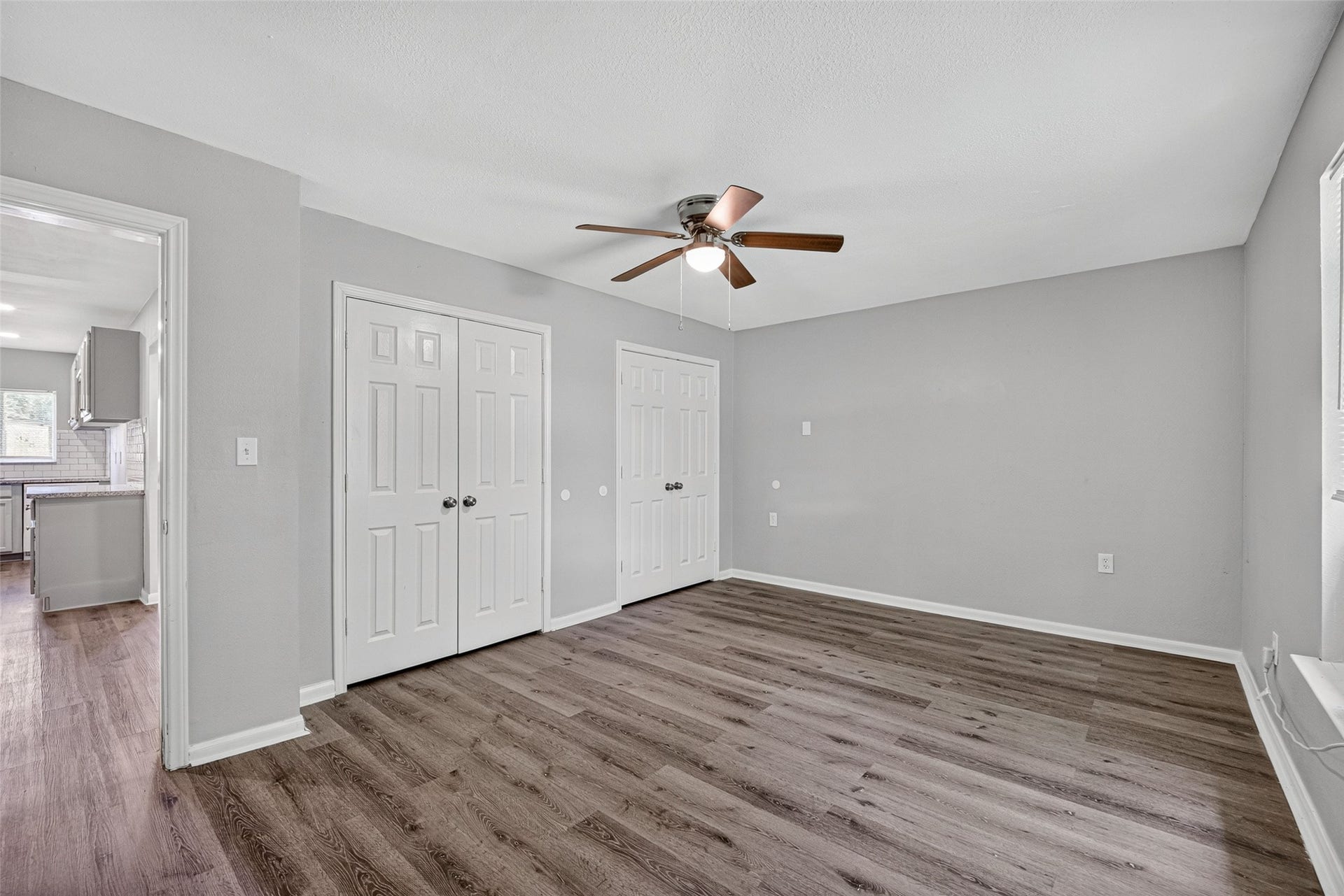3408 Palm Avenue, Texas City, TX 77590 Here's a concise and compelling description for a home buyer:
"Discover this spacious room with elegant wood-look flooring and neutral gray walls. It features a ceiling fan, two double-door closets, and an open doorway leading to a bright kitchen with modern cabinetry.