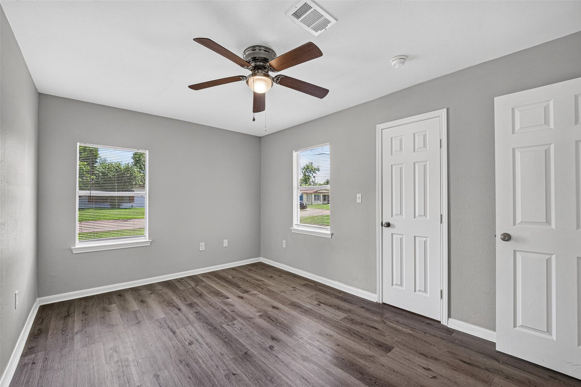 3408 Palm Avenue, Texas City, TX 77590 This room features a modern, neutral design with gray walls and dark wood flooring. It has two windows for natural light, a ceiling fan, and a closet with white doors.