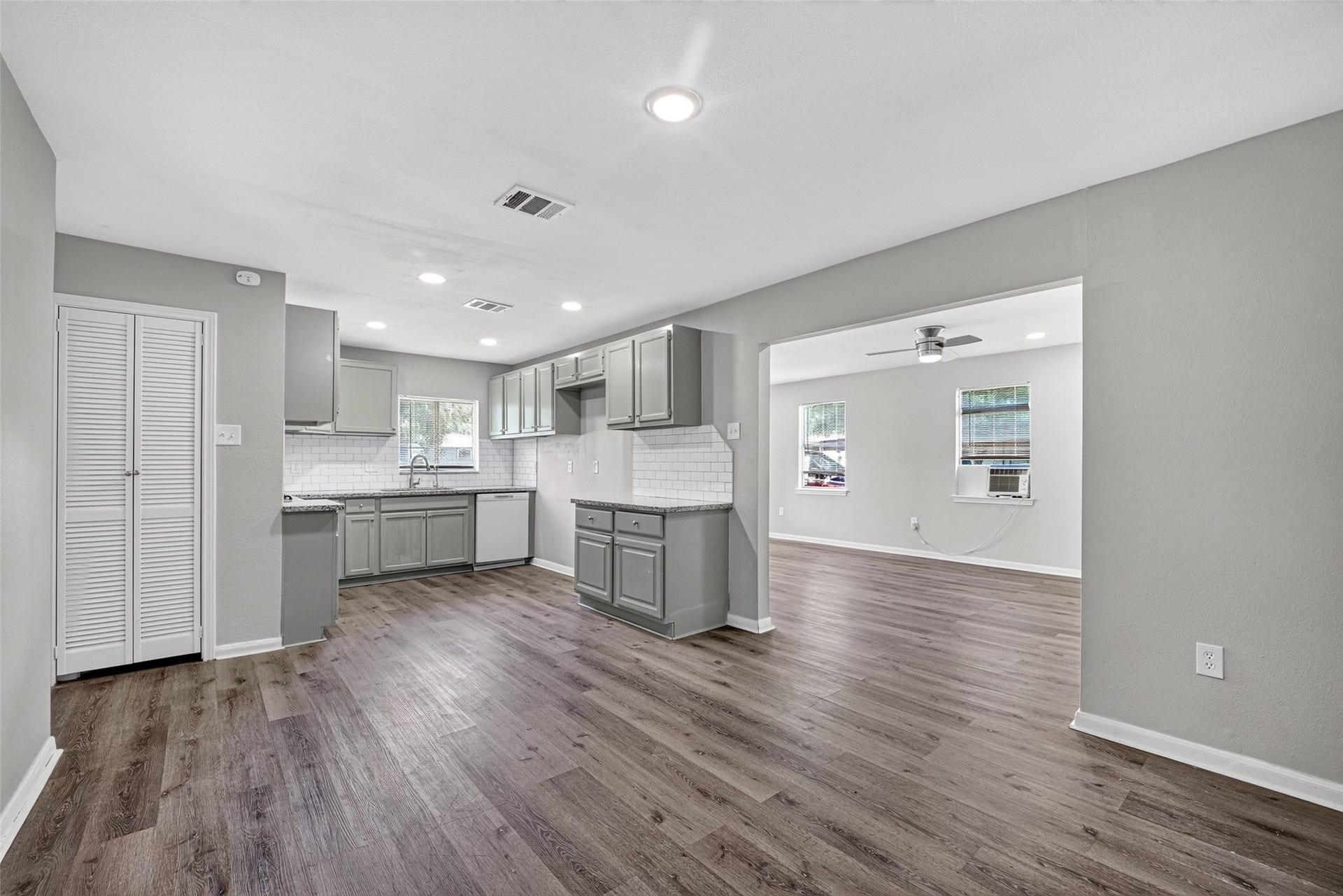 3408 Palm Avenue, Texas City, TX 77590 Experience modern living in this open-concept kitchen and living area, featuring sleek gray cabinetry, elegant hardwood flooring, and abundant natural light. The kitchen boasts a stylish white tile backsplash and recessed lighting, seamlessly flowing into a bright living space with large windows and a ceiling fan.