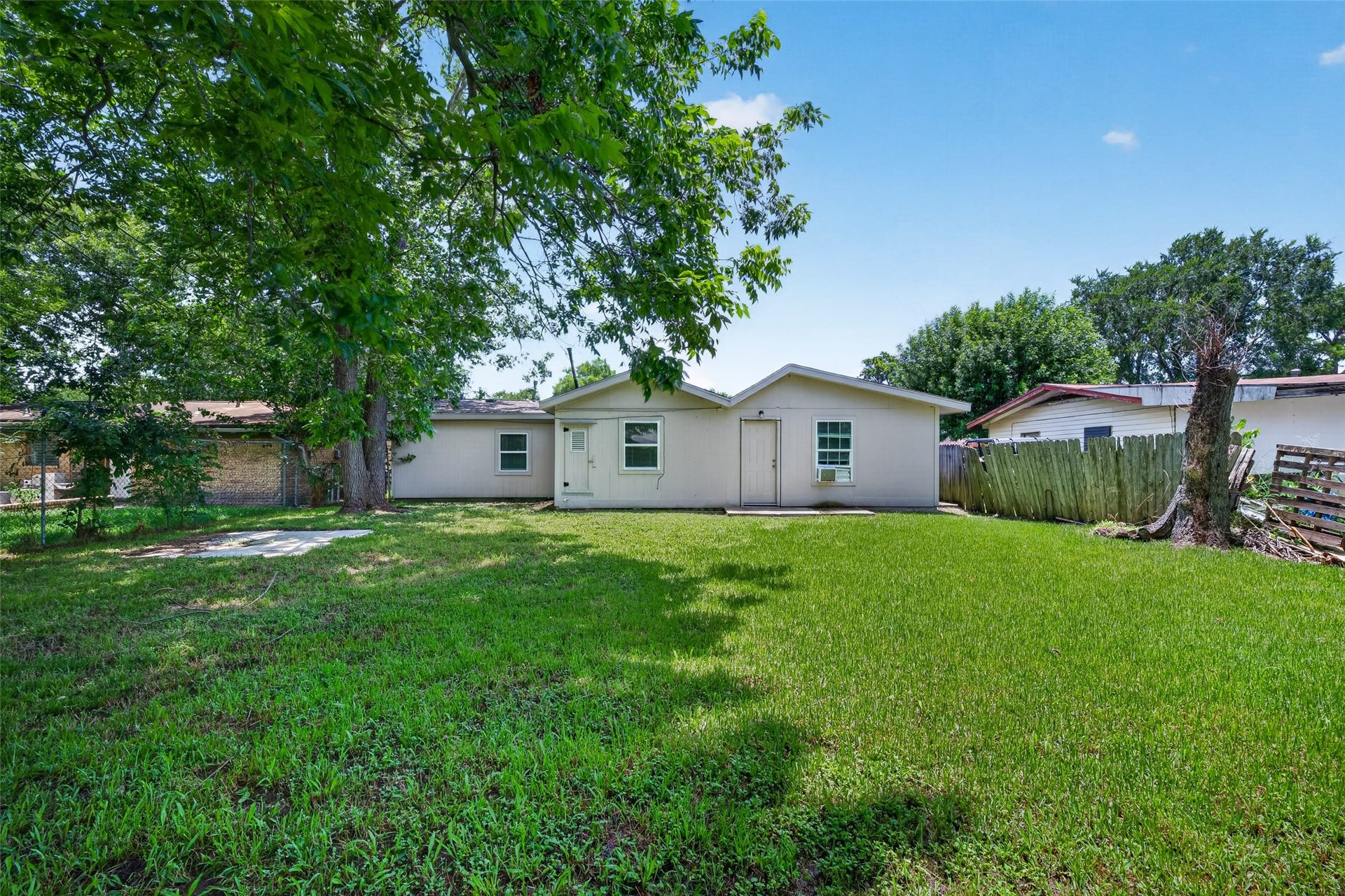 3408 Palm Avenue, Texas City, TX 77590 Charming backyard with lush grass, mature trees, and a cozy single-story house. Fenced for privacy, offering ample space for outdoor activities.